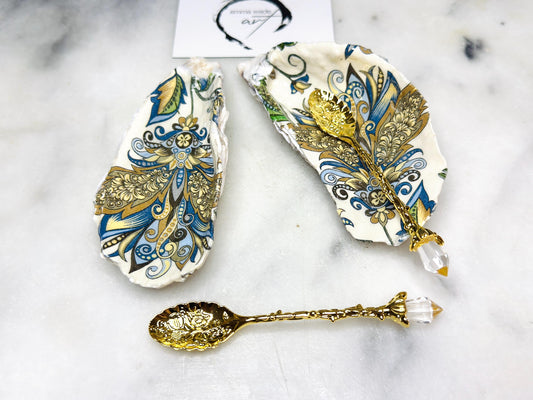 Handmade oyster shell salt and pepper dishes decorated in an elegant baroque gold design, shown as a matching pair with two gold spoons on a light marble background. Natural Dorset shells turned into coastal-inspired pinch pots, perfect for luxury table decor, wedding tables, or a unique hostess gift. Each shell is individually crafted, glossy finished, and one of a kind.