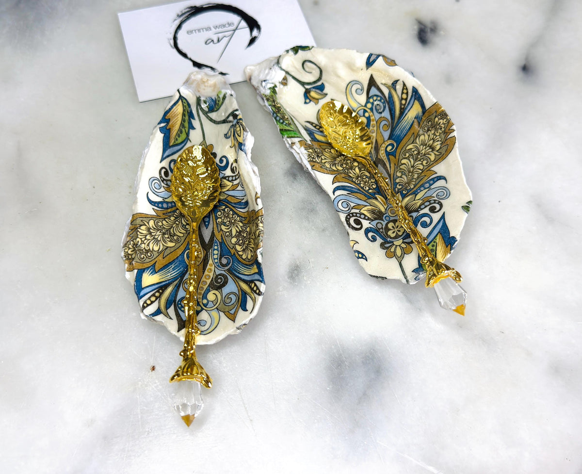 Handmade oyster shell salt and pepper dishes decorated in an elegant baroque gold design, shown as a matching pair with two gold spoons on a light marble background. Natural Dorset shells turned into coastal-inspired pinch pots, perfect for luxury table decor, wedding tables, or a unique hostess gift. Each shell is individually crafted, glossy finished, and one of a kind.
