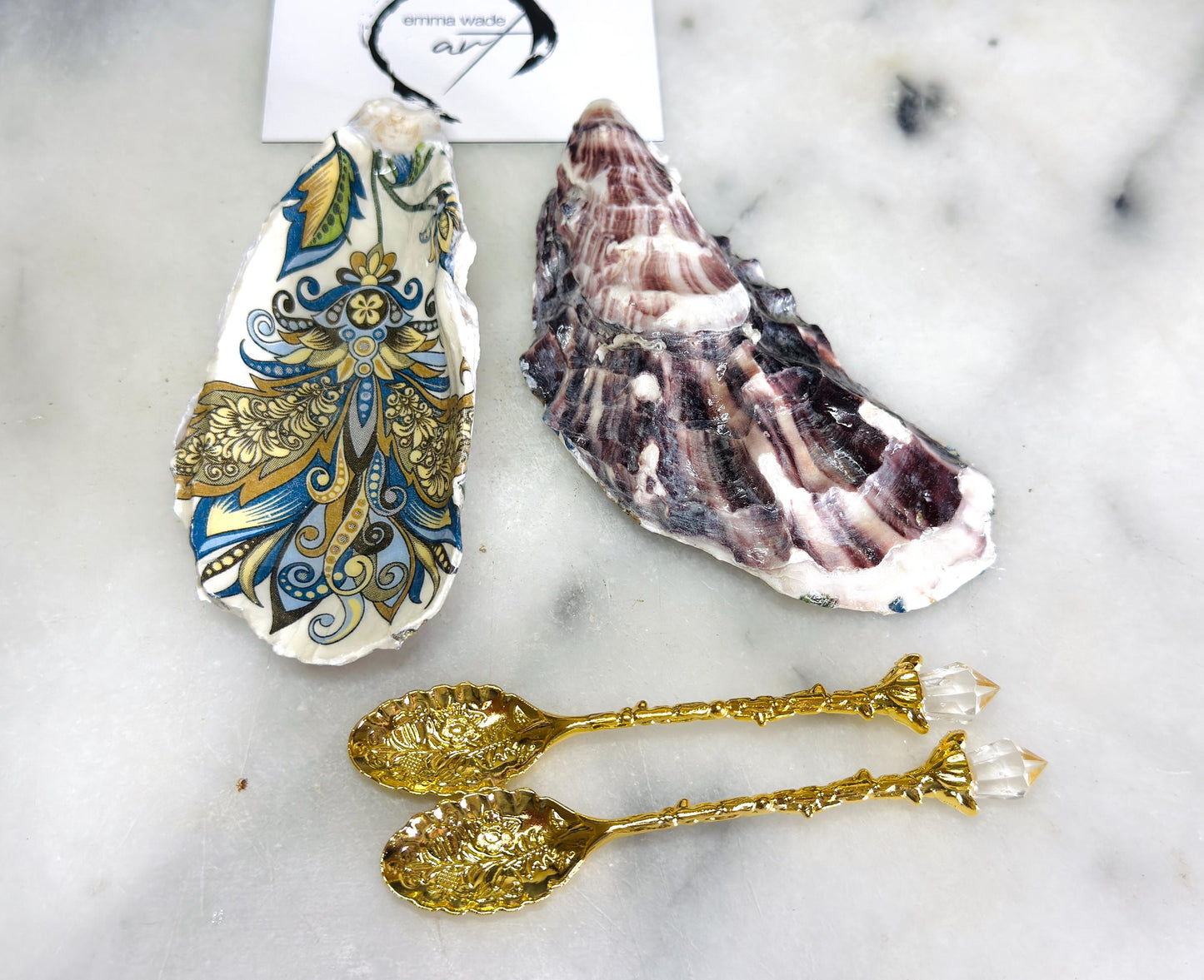 Handmade oyster shell salt and pepper dishes decorated in an elegant baroque gold design, shown as a matching pair with two gold spoons on a light marble background. Natural Dorset shells turned into coastal-inspired pinch pots, perfect for luxury table decor, wedding tables, or a unique hostess gift. Each shell is individually crafted, glossy finished, and one of a kind.