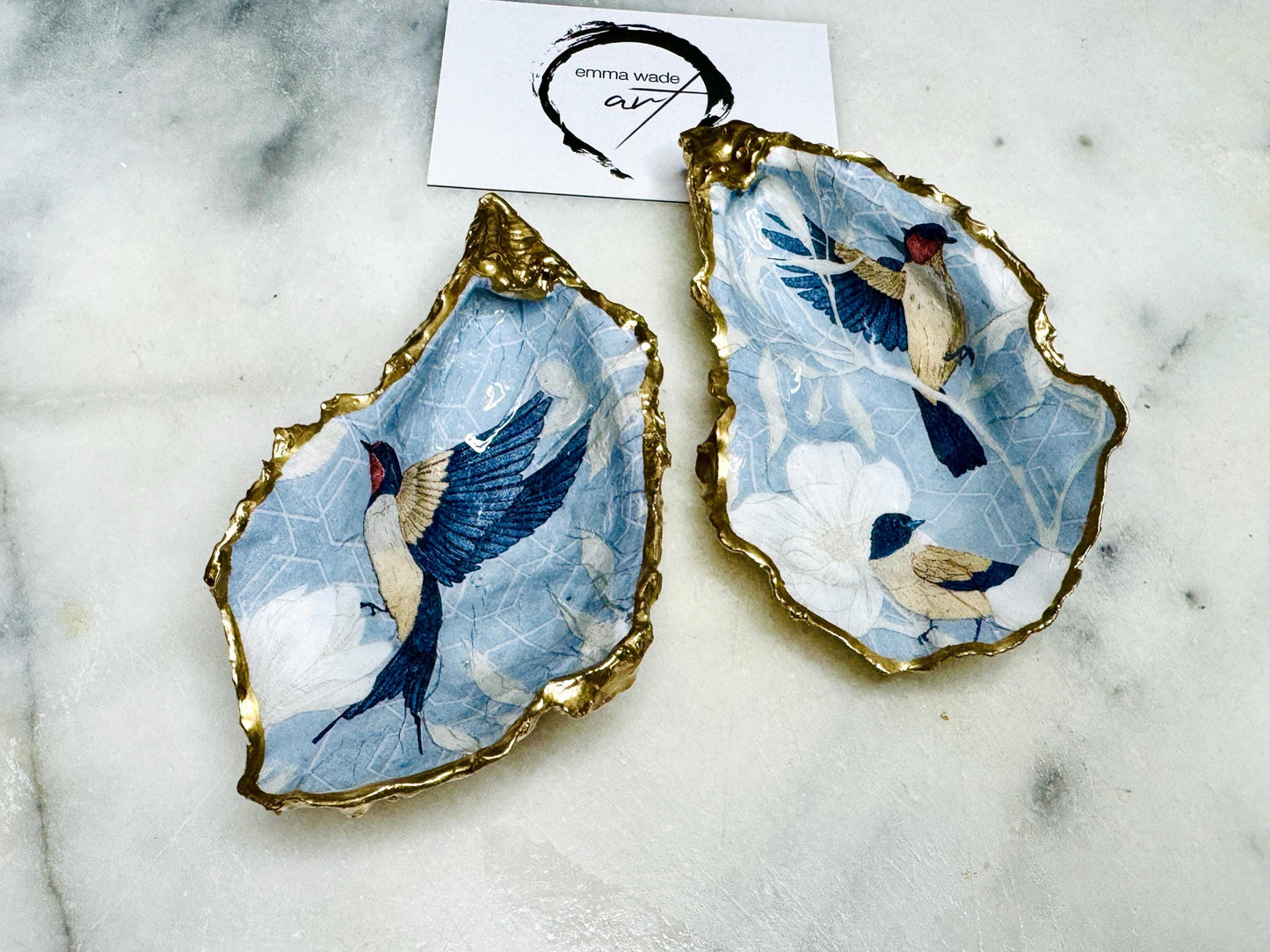 Handmade blue bird oyster shell salt and pepper dishes shown as a matching pair without spoons, featuring a delicate bird design and hand-gilded gold leaf edges. Crafted from natural Dorset oyster shells and sealed with a glossy finish, these coastal-inspired pinch pots are perfect for elegant table decor, weddings, or a unique hostess gift. Each shell is one of a kind and finished by hand.