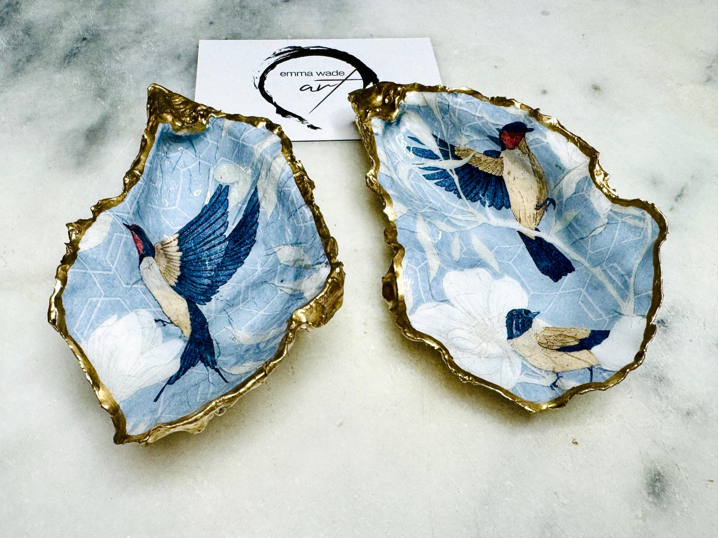 Handmade blue bird oyster shell salt and pepper dishes shown as a matching pair without spoons, featuring a delicate bird design and hand-gilded gold leaf edges. Crafted from natural Dorset oyster shells and sealed with a glossy finish, these coastal-inspired pinch pots are perfect for elegant table decor, weddings, or a unique hostess gift. Each shell is one of a kind and finished by hand.