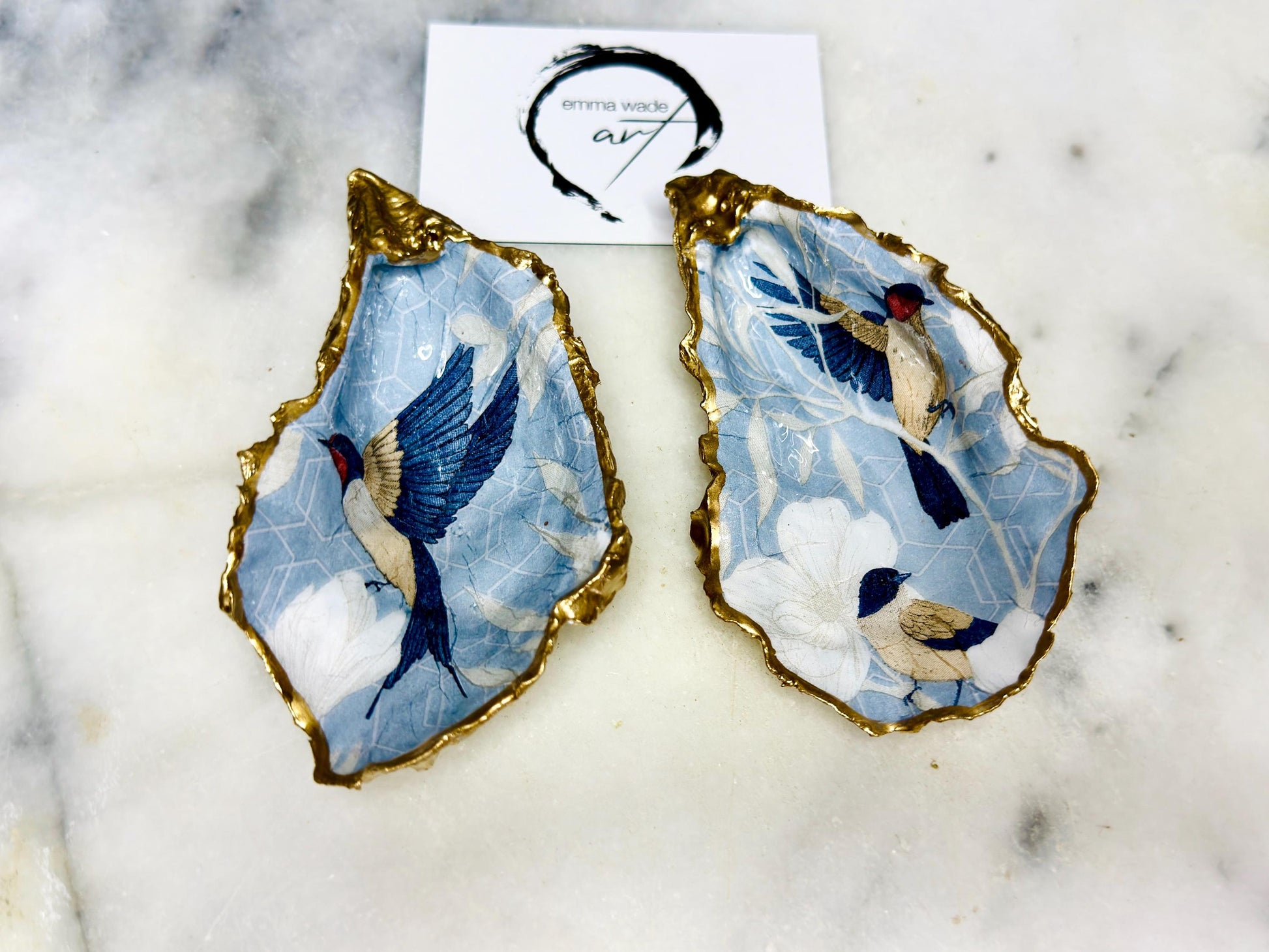 Handmade blue bird oyster shell salt and pepper dishes shown as a matching pair without spoons, featuring a delicate bird design and hand-gilded gold leaf edges. Crafted from natural Dorset oyster shells and sealed with a glossy finish, these coastal-inspired pinch pots are perfect for elegant table decor, weddings, or a unique hostess gift. Each shell is one of a kind and finished by hand.