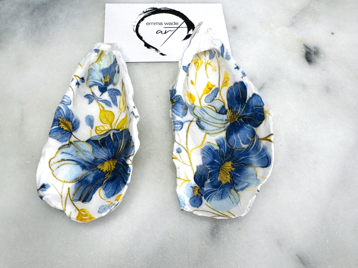 Handmade blue and yellow floral oyster shell salt and pepper dishes shown as a matching pair, crafted from natural Dorset shells and styled with small gold spoons. Coastal-inspired pinch pots featuring a decorative floral design with natural shell backs, perfect for table decor, weddings, or a unique hostess gift. Each shell is one of a kind, finished by hand, and ideal for adding colour and elegance to a dining table.