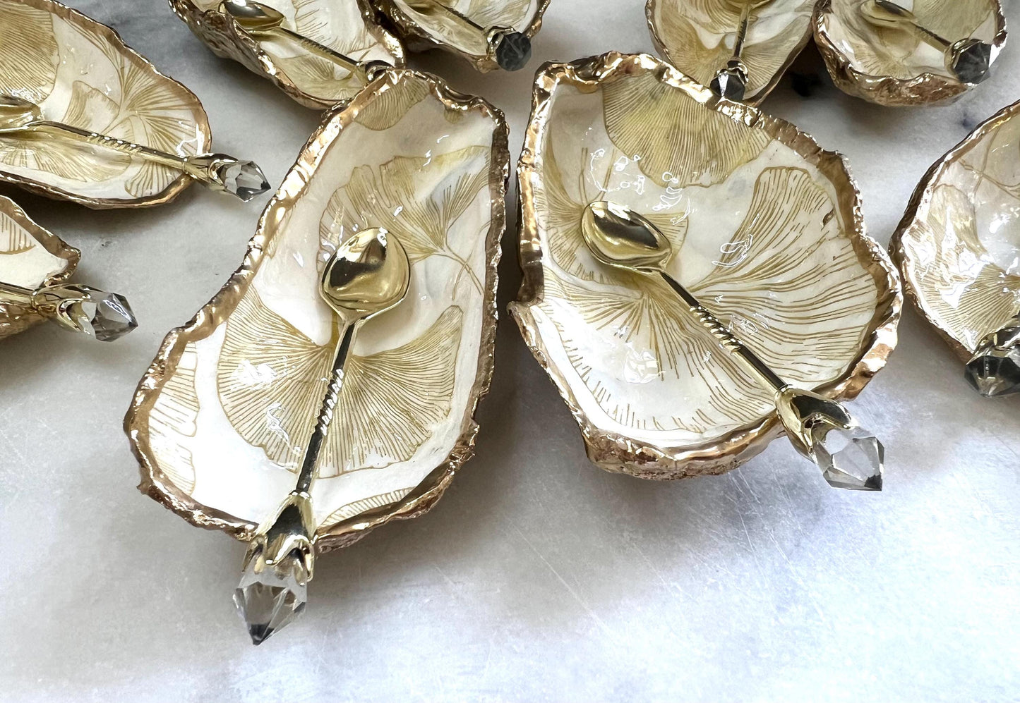 Pair of handmade Dorset oyster shell salt and pepper pinch pots featuring elegant Japanese Ginkgo floral artwork in soft gold and pearl tones with hand-applied gold leaf edging. Coastal luxury cruet set sealed in glossy Crystal resin with optional gold crystal spoons.