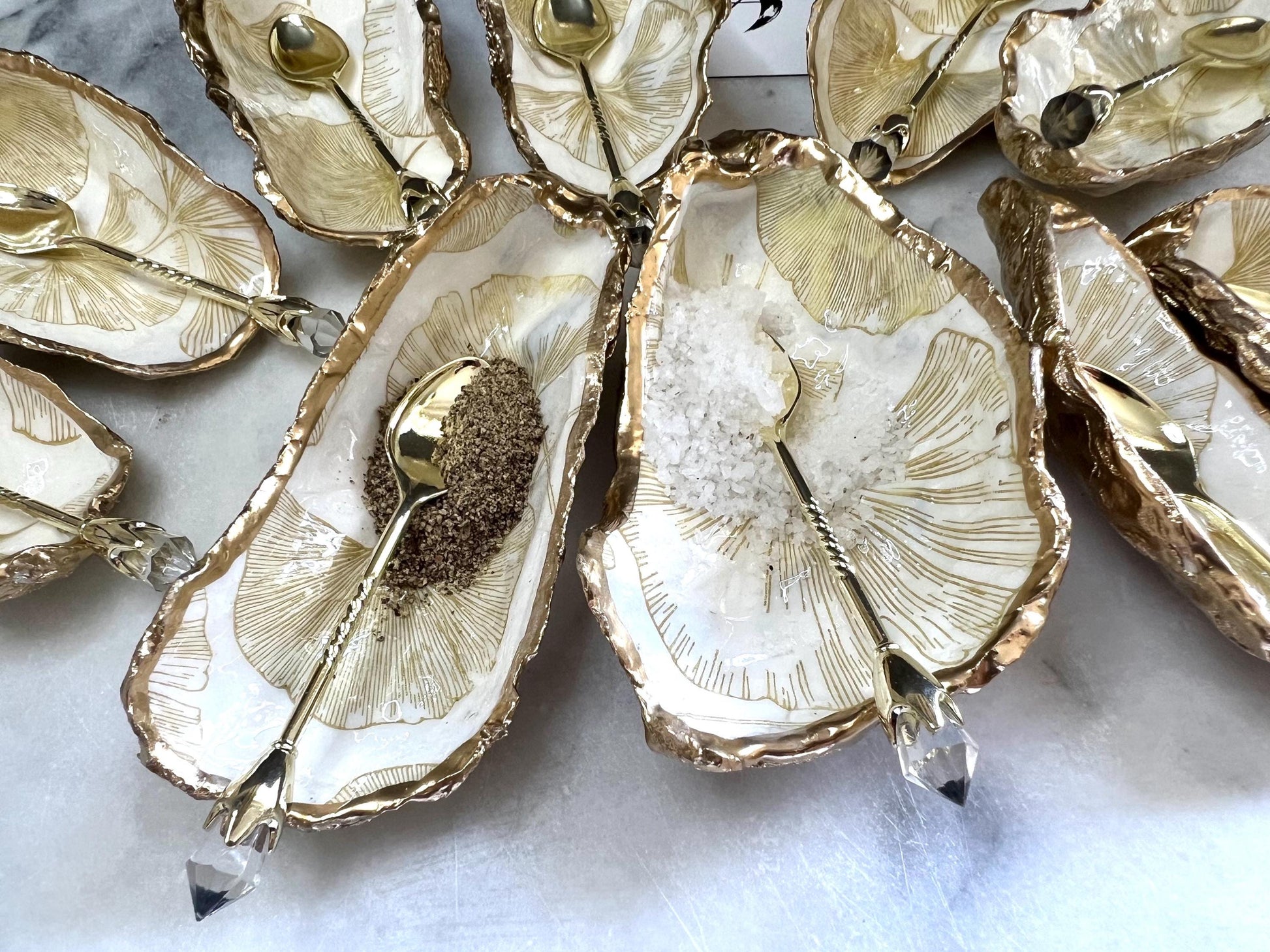 Pair of handmade Dorset oyster shell salt and pepper pinch pots featuring elegant Japanese Ginkgo floral artwork in soft gold and pearl tones with hand-applied gold leaf edging. Coastal luxury cruet set sealed in glossy Crystal resin with optional gold crystal spoons.