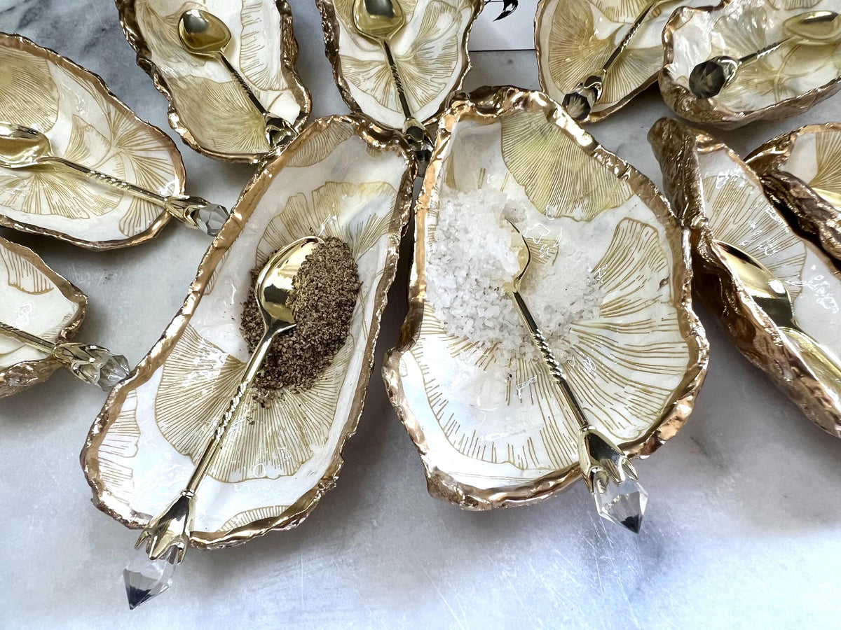 Pair of handmade Dorset oyster shell salt and pepper pinch pots featuring elegant Japanese Ginkgo floral artwork in soft gold and pearl tones with hand-applied gold leaf edging. Coastal luxury cruet set sealed in glossy Crystal resin with optional gold crystal spoons.