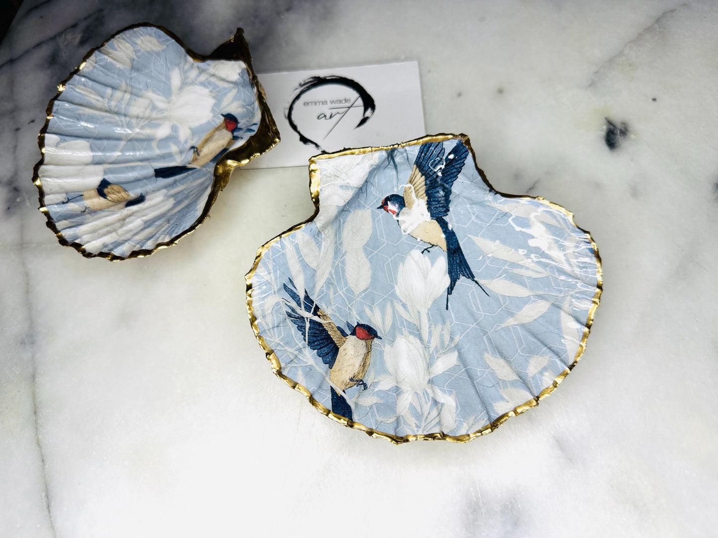 Handmade scallop shell trinket dish featuring a Blue Birds of Paradise decoupage design, finished with real gold leaf and sealed with glossy resin. Crafted from a natural Dorset scallop shell and shown as a jewellery and ring holder on a light background. Coastal-inspired home decor, perfect for holding rings, earrings and small keepsakes, with each shell one of a kind and finished by hand.