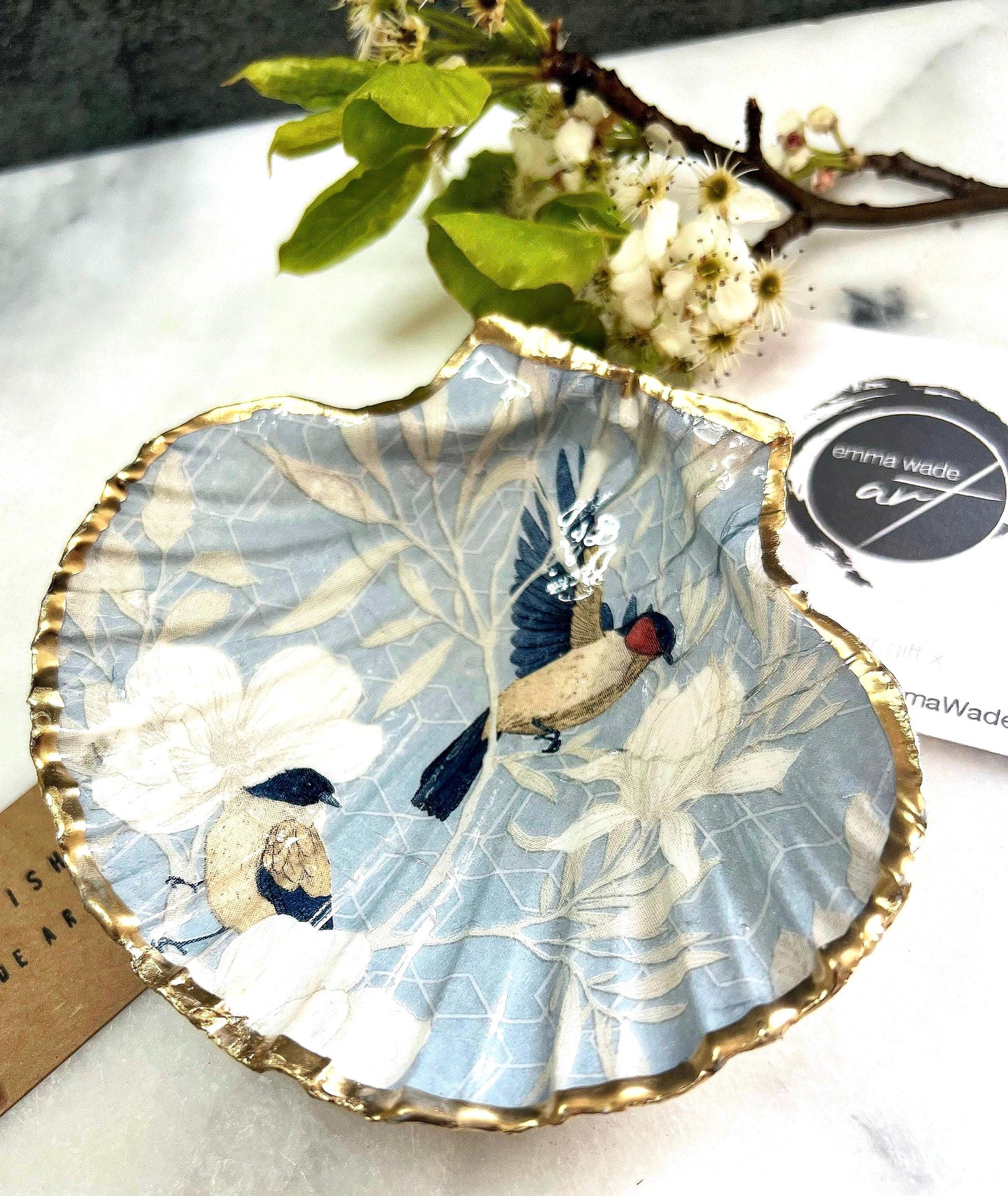 Handmade scallop shell trinket dish featuring a Blue Birds of Paradise decoupage design, finished with real gold leaf and sealed with glossy resin. Crafted from a natural Dorset scallop shell and shown as a jewellery and ring holder on a light background. Coastal-inspired home decor, perfect for holding rings, earrings and small keepsakes, with each shell one of a kind and finished by hand.