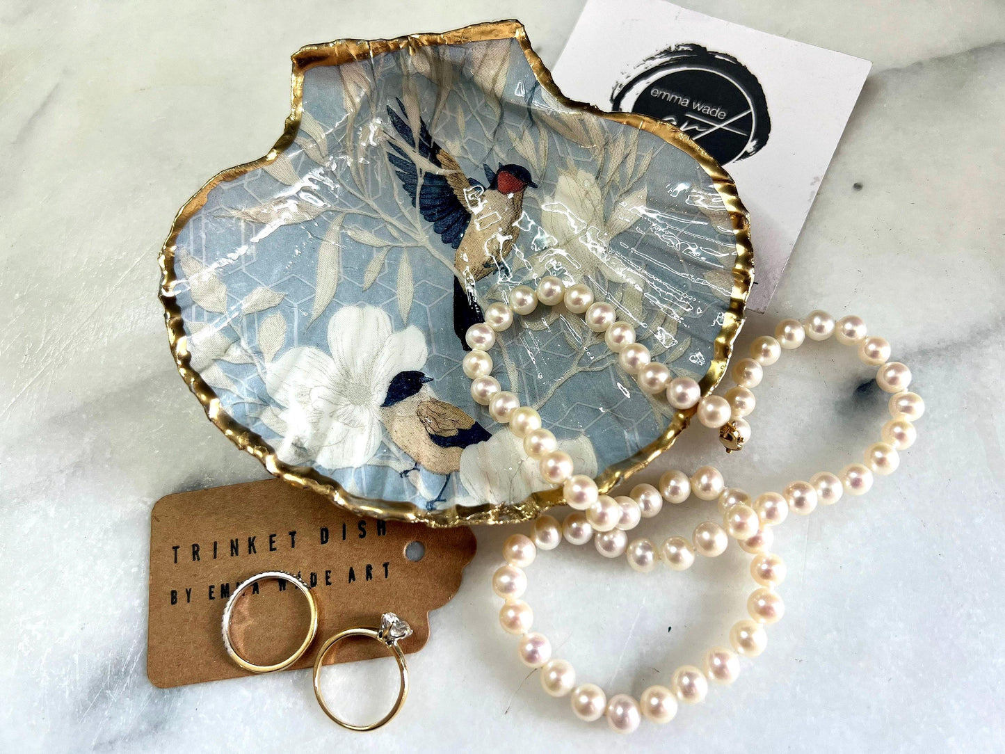 Handmade scallop shell trinket dish featuring a Blue Birds of Paradise decoupage design, finished with real gold leaf and sealed with glossy resin. Crafted from a natural Dorset scallop shell and shown as a jewellery and ring holder on a light background. Coastal-inspired home decor, perfect for holding rings, earrings and small keepsakes, with each shell one of a kind and finished by hand.