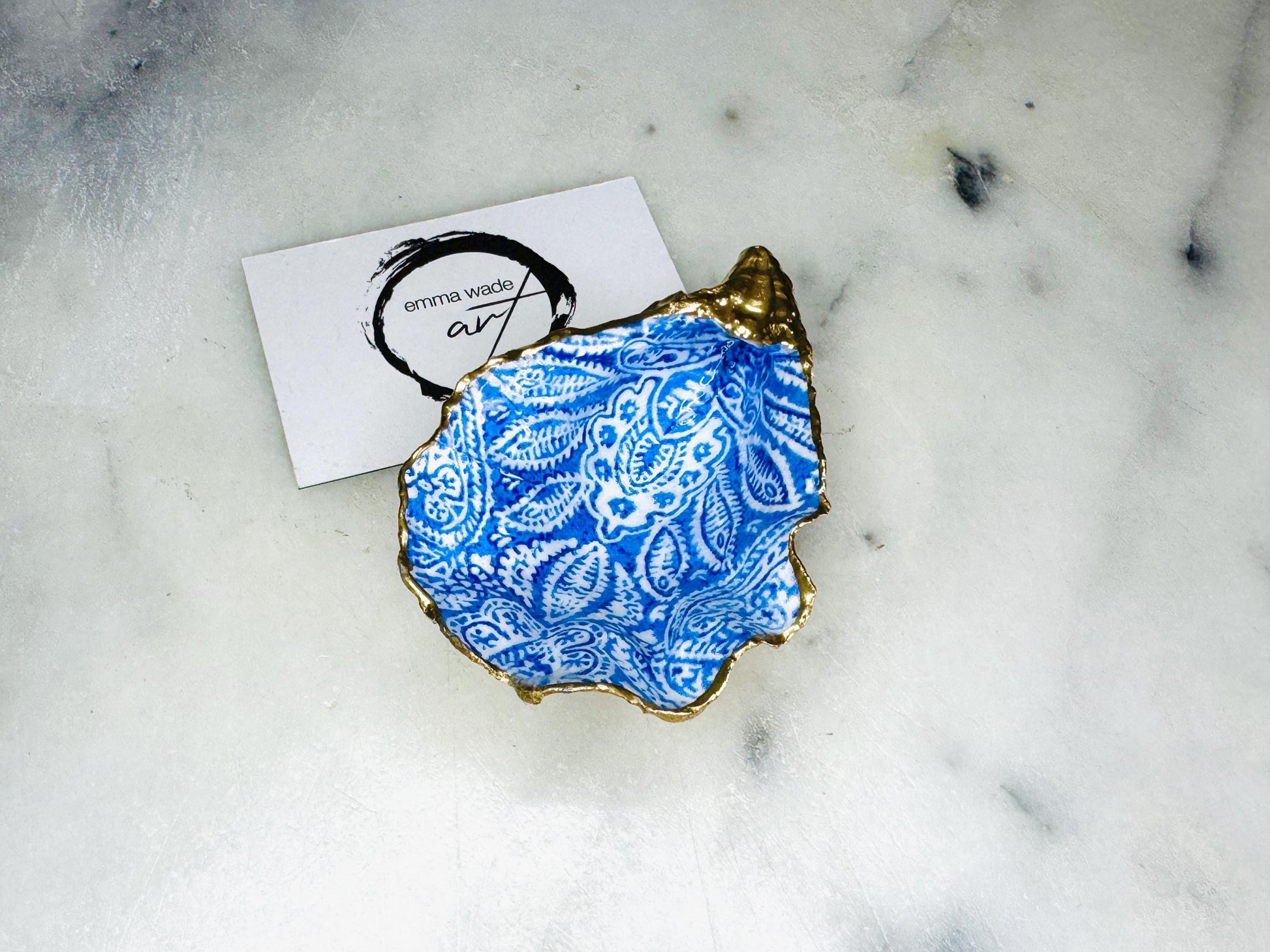 Handmade Dorset oyster shell trinket dish featuring an elegant blue and white paisley design, hand-gilded with liquid gold leaf and finished in glossy resin. Coastal shell jewellery holder available in multiple sizes from small to XL, ideal as a ring dish, trinket tray, vanity decor, or luxury coastal gift.