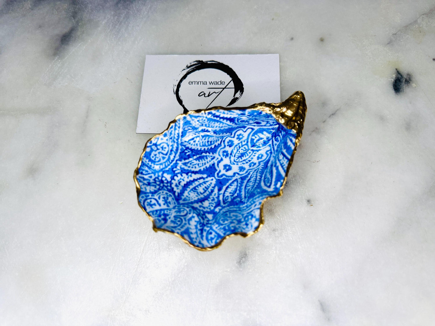 Handmade Dorset oyster shell trinket dish featuring an elegant blue and white paisley design, hand-gilded with liquid gold leaf and finished in glossy resin. Coastal shell jewellery holder available in multiple sizes from small to XL, ideal as a ring dish, trinket tray, vanity decor, or luxury coastal gift.