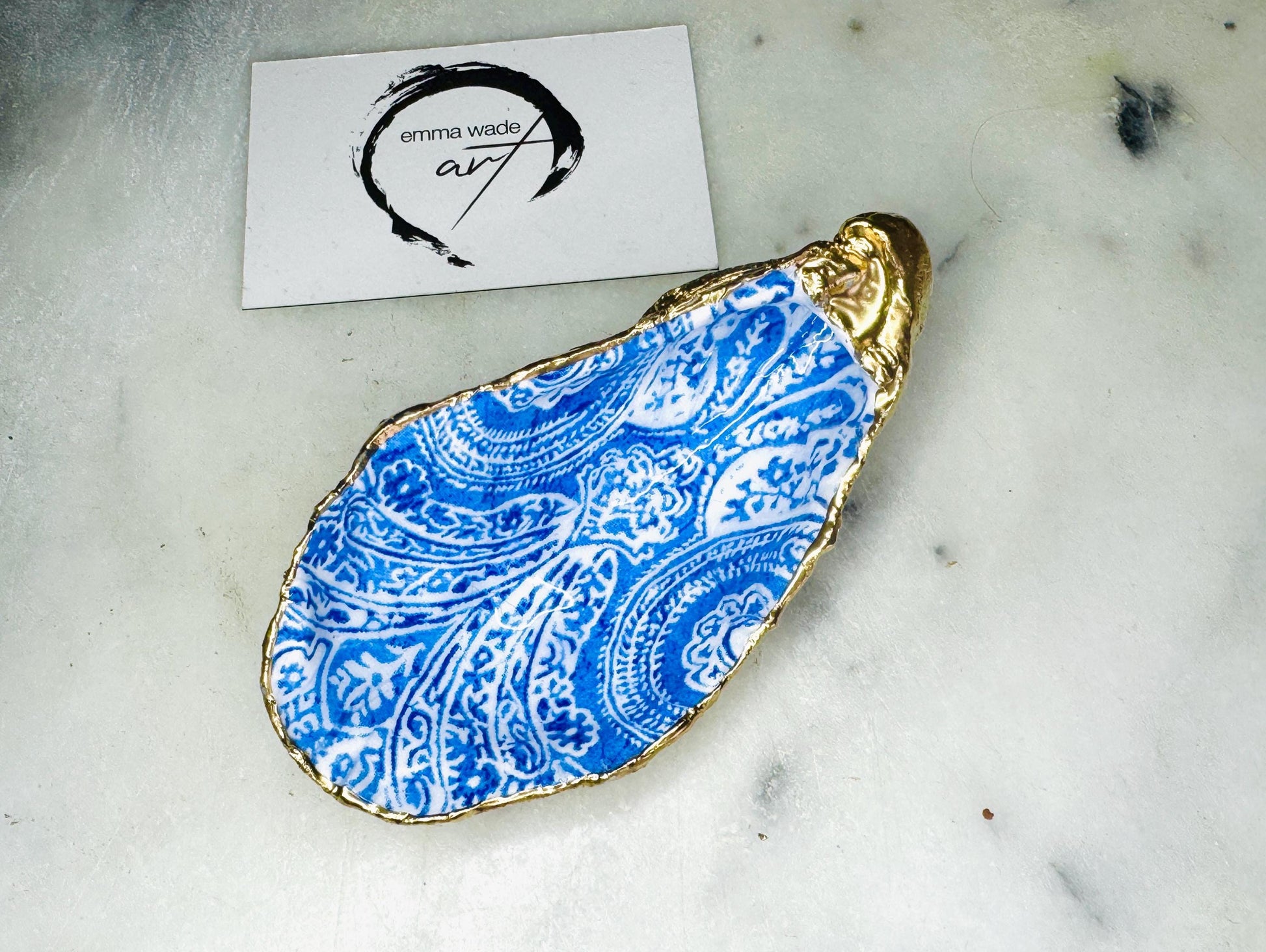 Handmade Dorset oyster shell trinket dish featuring an elegant blue and white paisley design, hand-gilded with liquid gold leaf and finished in glossy resin. Coastal shell jewellery holder available in multiple sizes from small to XL, ideal as a ring dish, trinket tray, vanity decor, or luxury coastal gift.