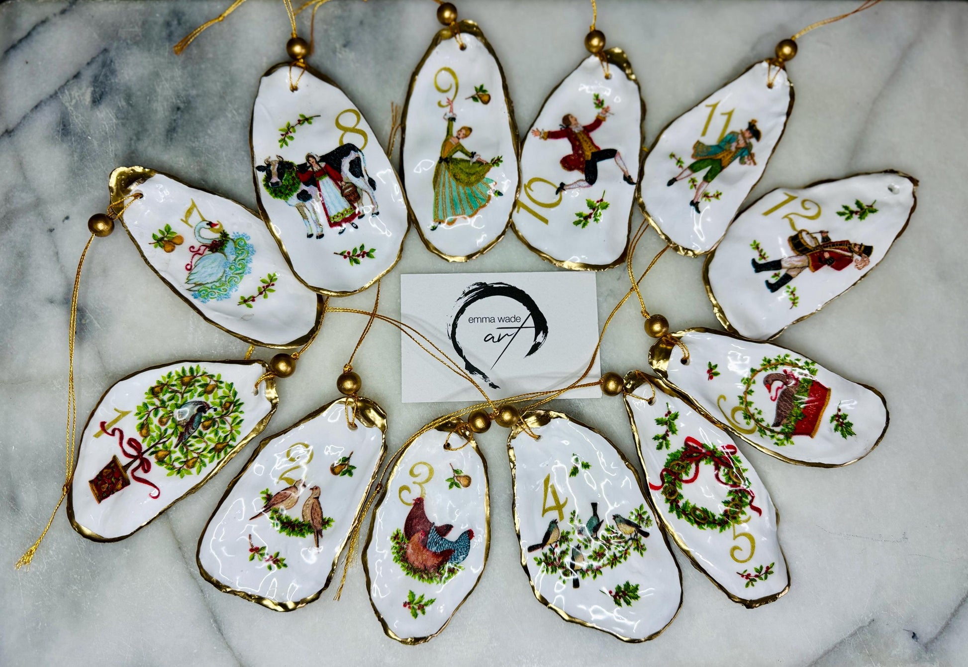 Handmade Twelve Days of Christmas oyster shell ornament set featuring all twelve traditional carol illustrations, finished with gold leaf edging, glossy resin and gold hanging cords. Coastal heirloom Christmas decorations handcrafted from Dorset oyster shells.