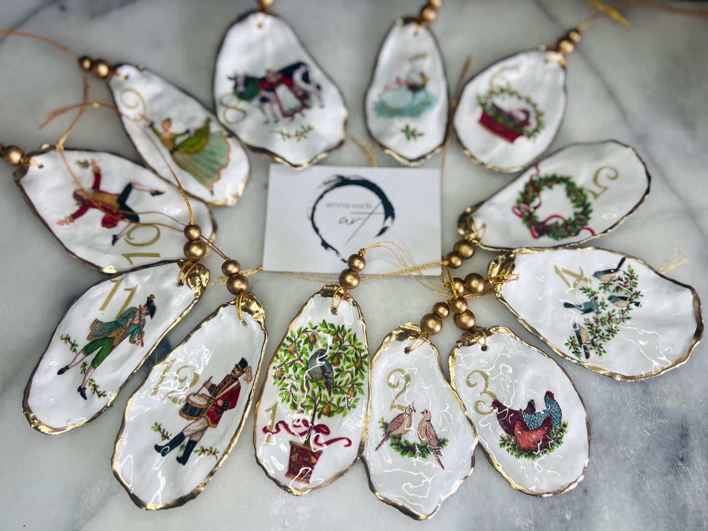 Handmade Twelve Days of Christmas oyster shell ornament set featuring all twelve traditional carol illustrations, finished with gold leaf edging, glossy resin and gold hanging cords. Coastal heirloom Christmas decorations handcrafted from Dorset oyster shells.