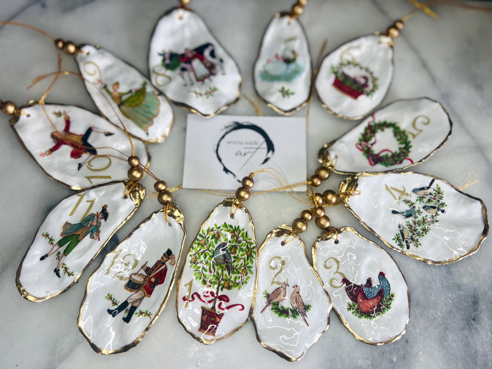 Handmade Twelve Days of Christmas oyster shell ornament set featuring all twelve traditional carol illustrations, finished with gold leaf edging, glossy resin and gold hanging cords. Coastal heirloom Christmas decorations handcrafted from Dorset oyster shells.