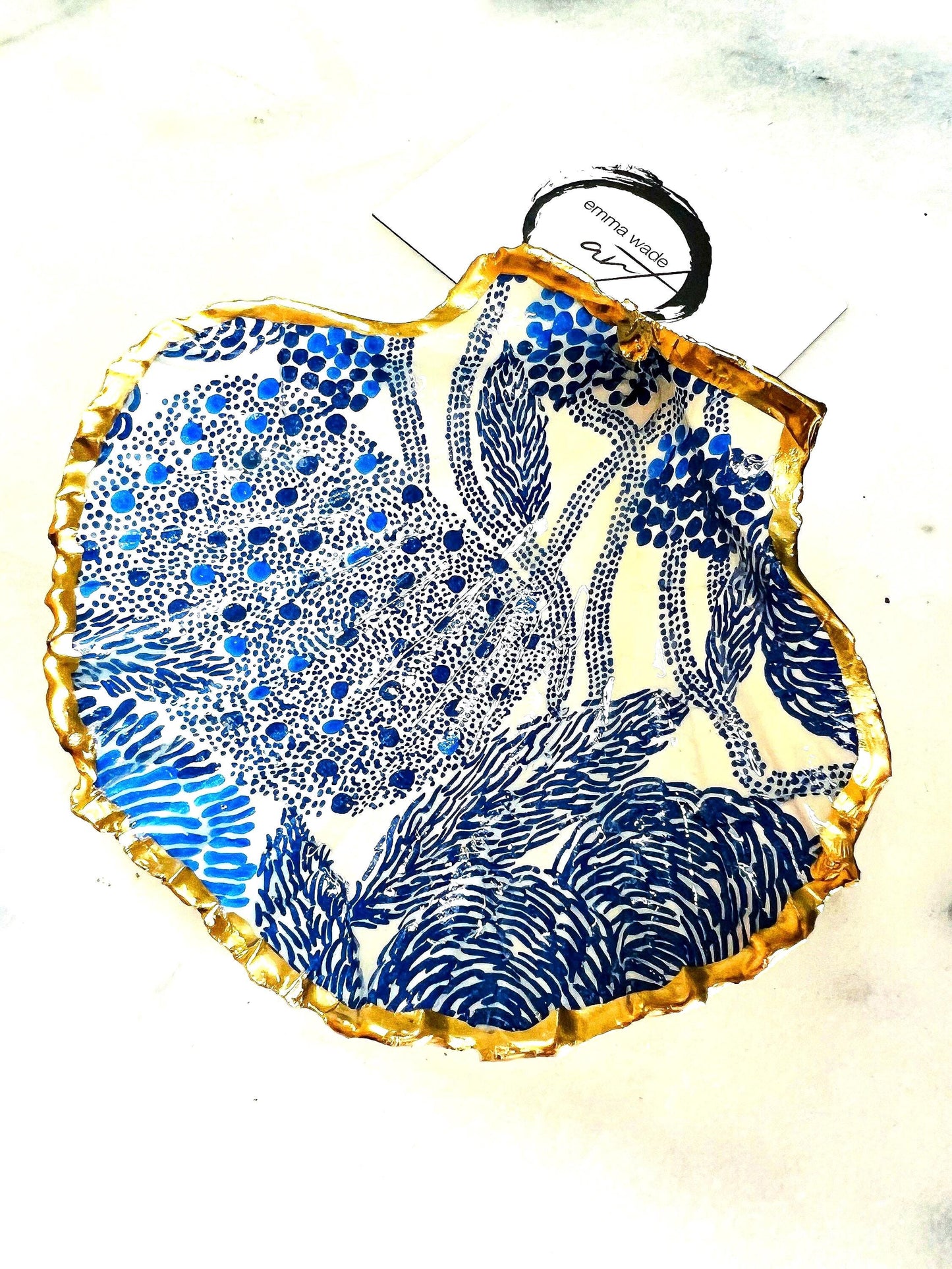 Marimekko inspired blue floral scallop shell trinket dish with hand-applied gold leaf edging and glossy resin finish. Natural Dorset shell jewellery holder featuring bold Scandinavian style botanical pattern. Decorative coastal ring dish styled on a marble surface, ideal as a bedside trinket bowl, host gift or luxury handmade home accent.