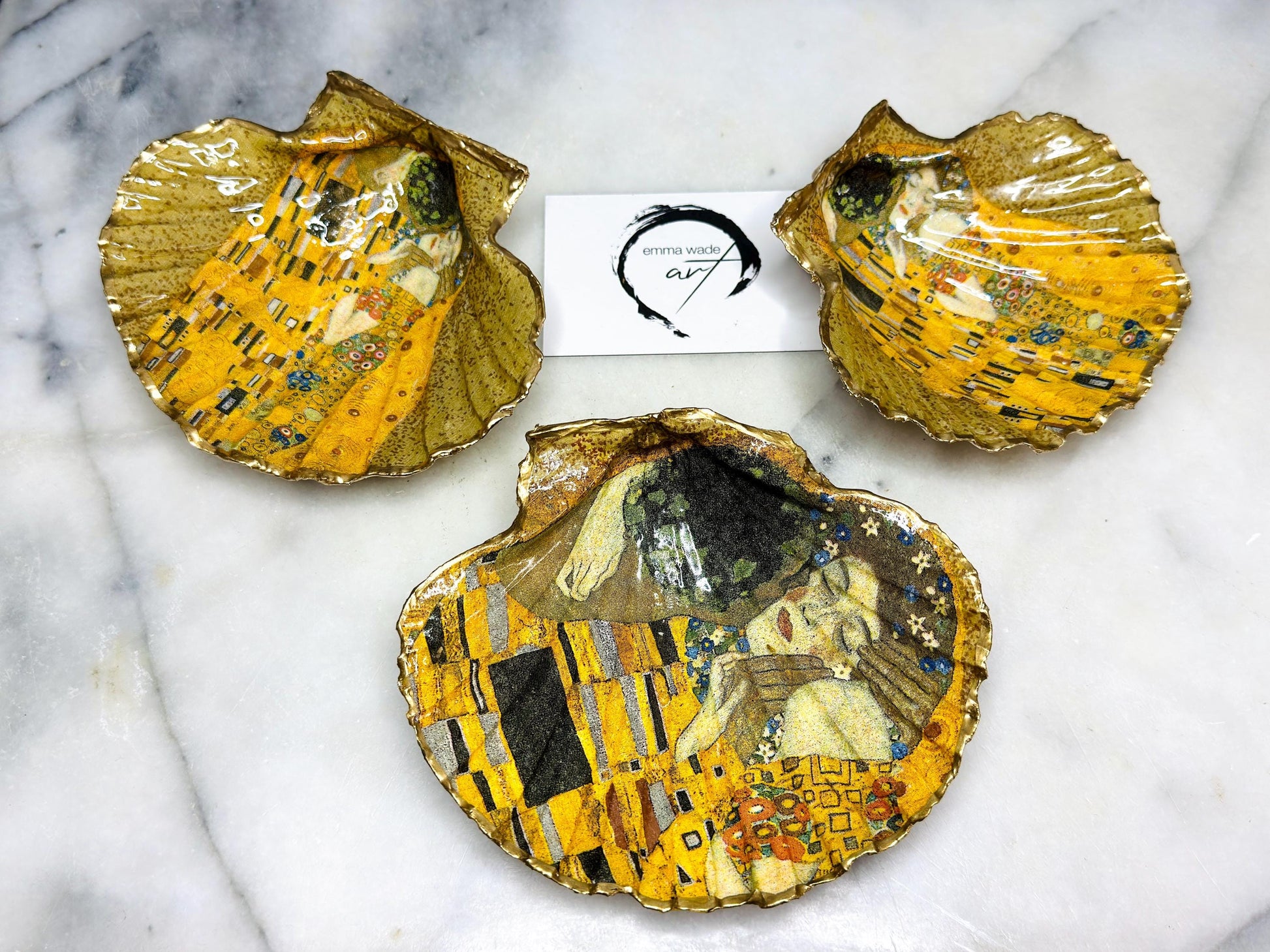 Handmade scallop shell trinket dish inspired by Gustav Klimt’s “The Kiss”, finished with gold leaf and sealed with glossy resin. Coastal Dorset shell jewellery dish perfect for rings, earrings and small treasures. Unique decorative shell bowl with golden artwork design, photographed on a light background showing detailed gilded surface and natural shell shape.