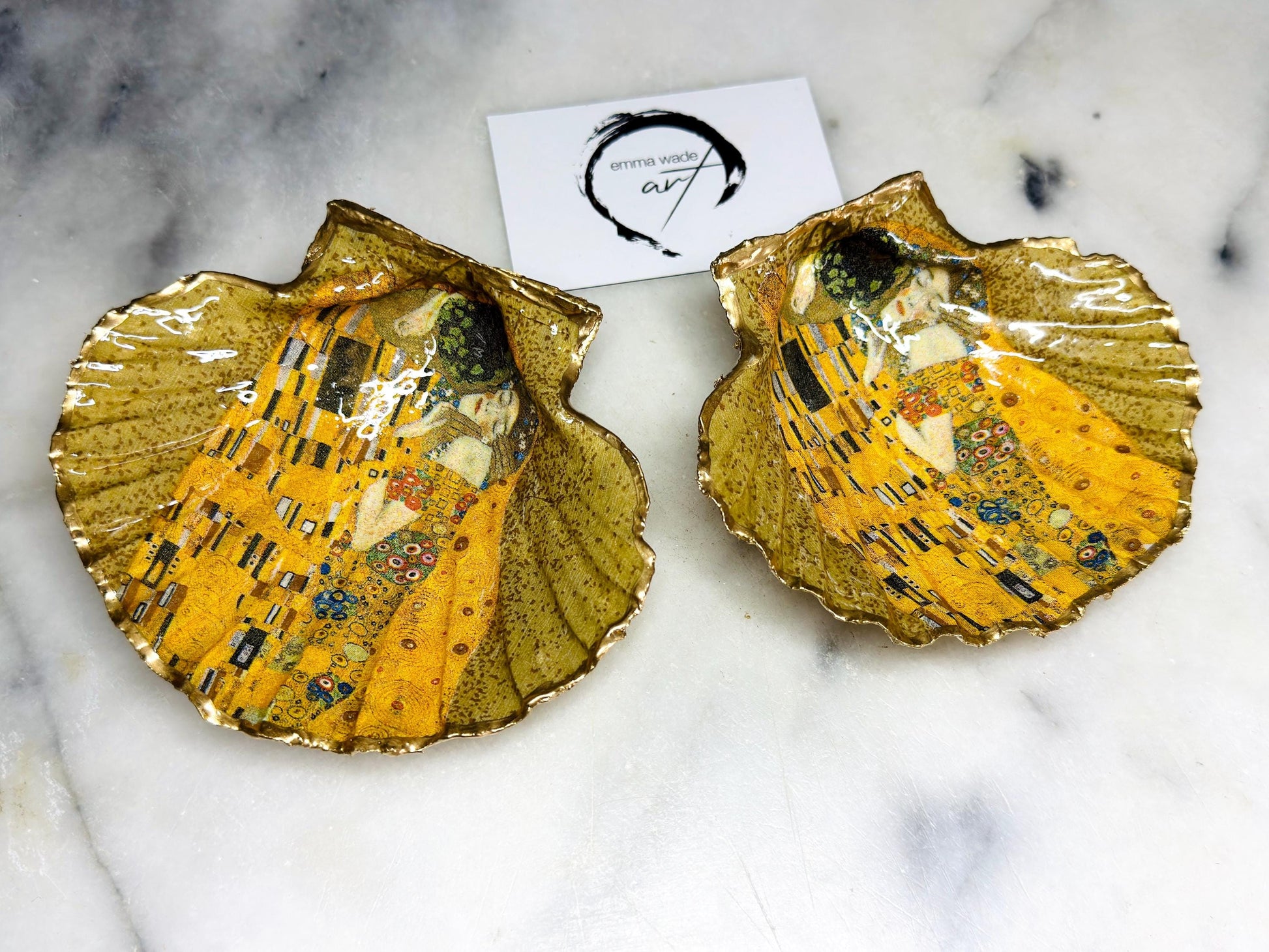 Handmade scallop shell trinket dish inspired by Gustav Klimt’s “The Kiss”, finished with gold leaf and sealed with glossy resin. Coastal Dorset shell jewellery dish perfect for rings, earrings and small treasures. Unique decorative shell bowl with golden artwork design, photographed on a light background showing detailed gilded surface and natural shell shape.