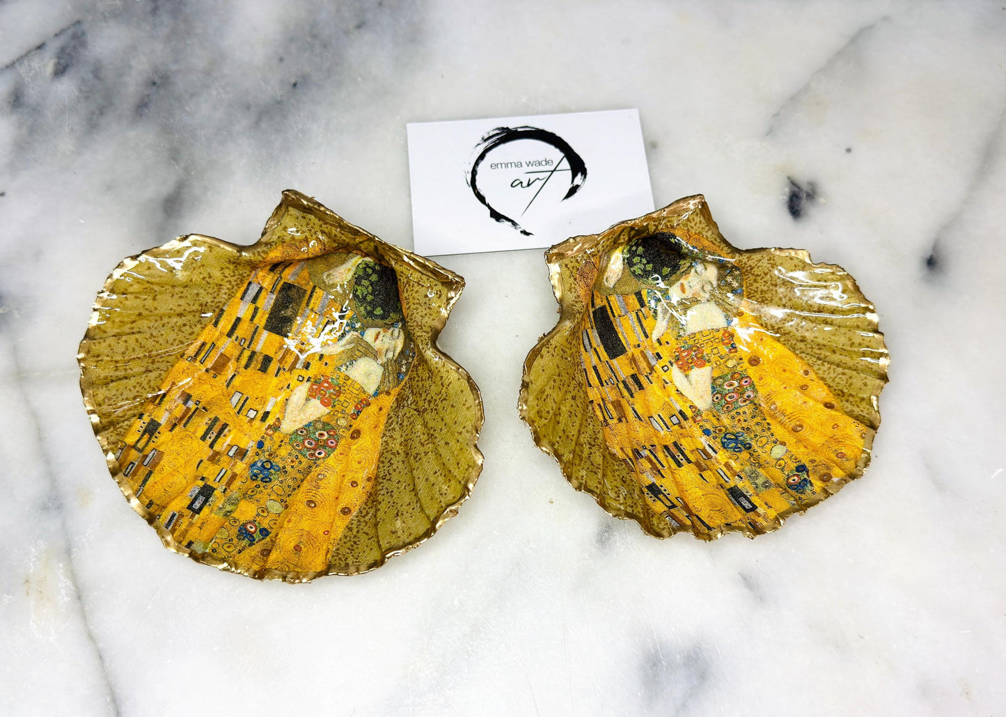 Handmade scallop shell trinket dish inspired by Gustav Klimt’s “The Kiss”, finished with gold leaf and sealed with glossy resin. Coastal Dorset shell jewellery dish perfect for rings, earrings and small treasures. Unique decorative shell bowl with golden artwork design, photographed on a light background showing detailed gilded surface and natural shell shape.