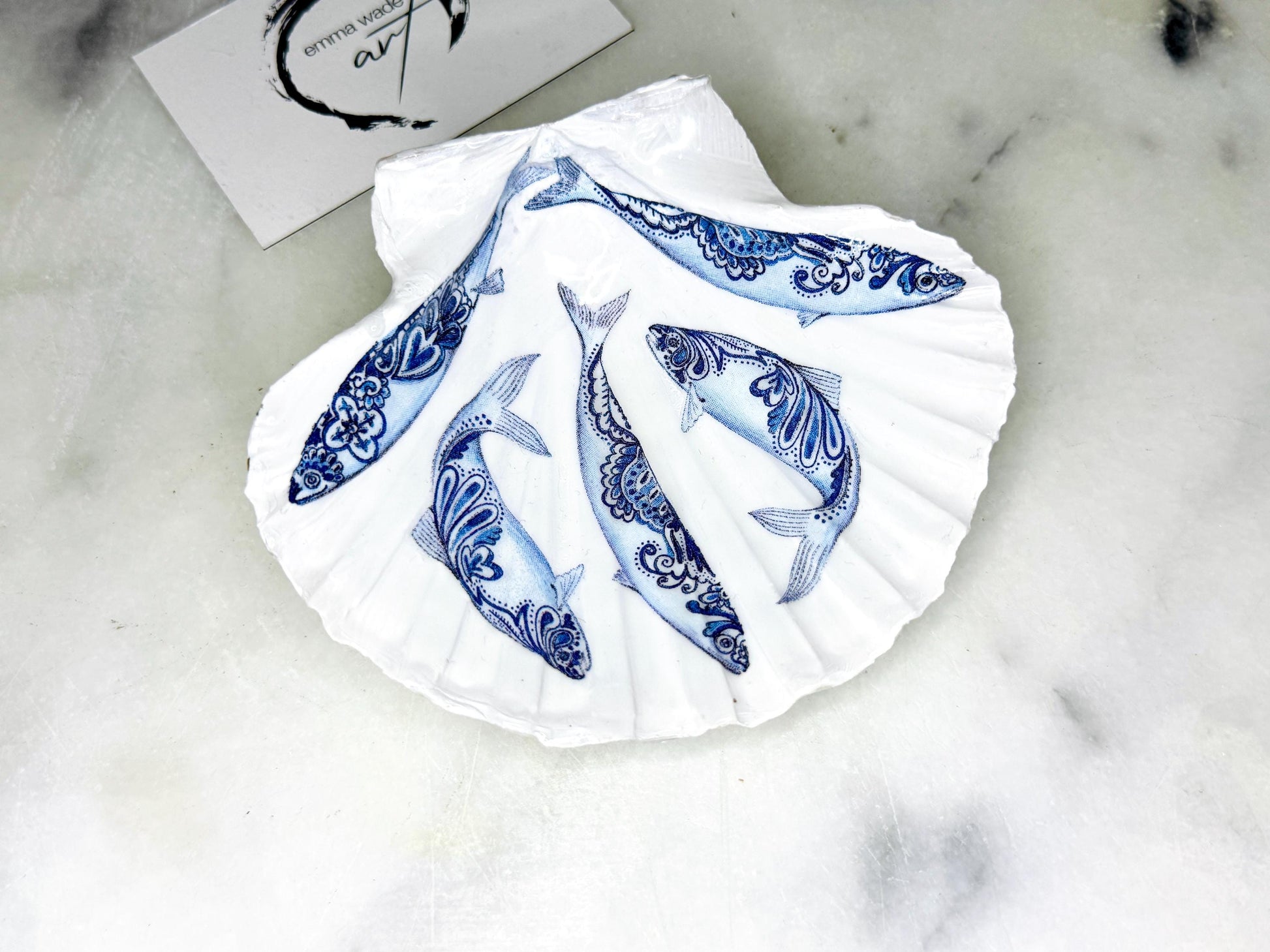 Handmade Dorset scallop shell trinket dishes featuring blue and white paisley fish illustrations with hand-painted gold leaf edging and glossy crystal clear resin. Coastal Scandinavian inspired jewellery dishes styled on a soft neutral background with elegant nautical fish artwork and luxurious gilded detailing.