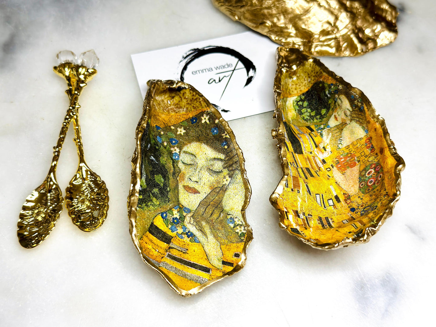 Pair of handmade Dorset oyster shell salt and pepper pinch pots inspired by Gustav Klimt’s The Kiss, decorated with rich gold artwork, hand-finished with liquid gold leaf, and sealed in crystal-hard glossy resin. Luxury coastal serving dishes with optional gold crystal spoons, perfect for weddings, anniversaries, dinner parties, and elegant table décor.