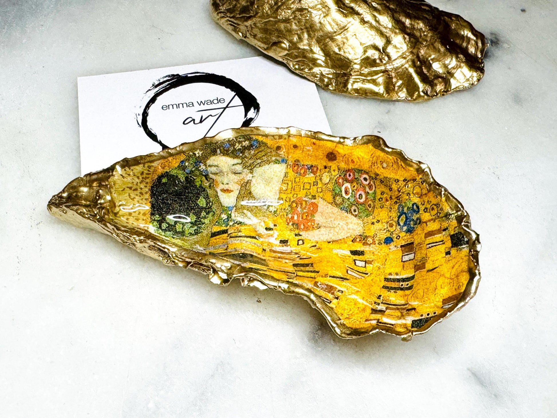 Pair of handmade Dorset oyster shell salt and pepper pinch pots inspired by Gustav Klimt’s The Kiss, decorated with rich gold artwork, hand-finished with liquid gold leaf, and sealed in crystal-hard glossy resin. Luxury coastal serving dishes with optional gold crystal spoons, perfect for weddings, anniversaries, dinner parties, and elegant table décor.