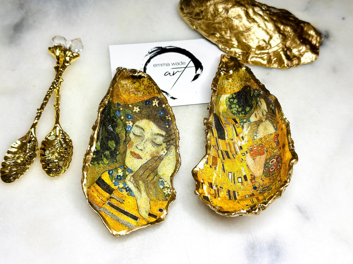 Pair of handmade Dorset oyster shell salt and pepper pinch pots inspired by Gustav Klimt’s The Kiss, decorated with rich gold artwork, hand-finished with liquid gold leaf, and sealed in crystal-hard glossy resin. Luxury coastal serving dishes with optional gold crystal spoons, perfect for weddings, anniversaries, dinner parties, and elegant table décor.