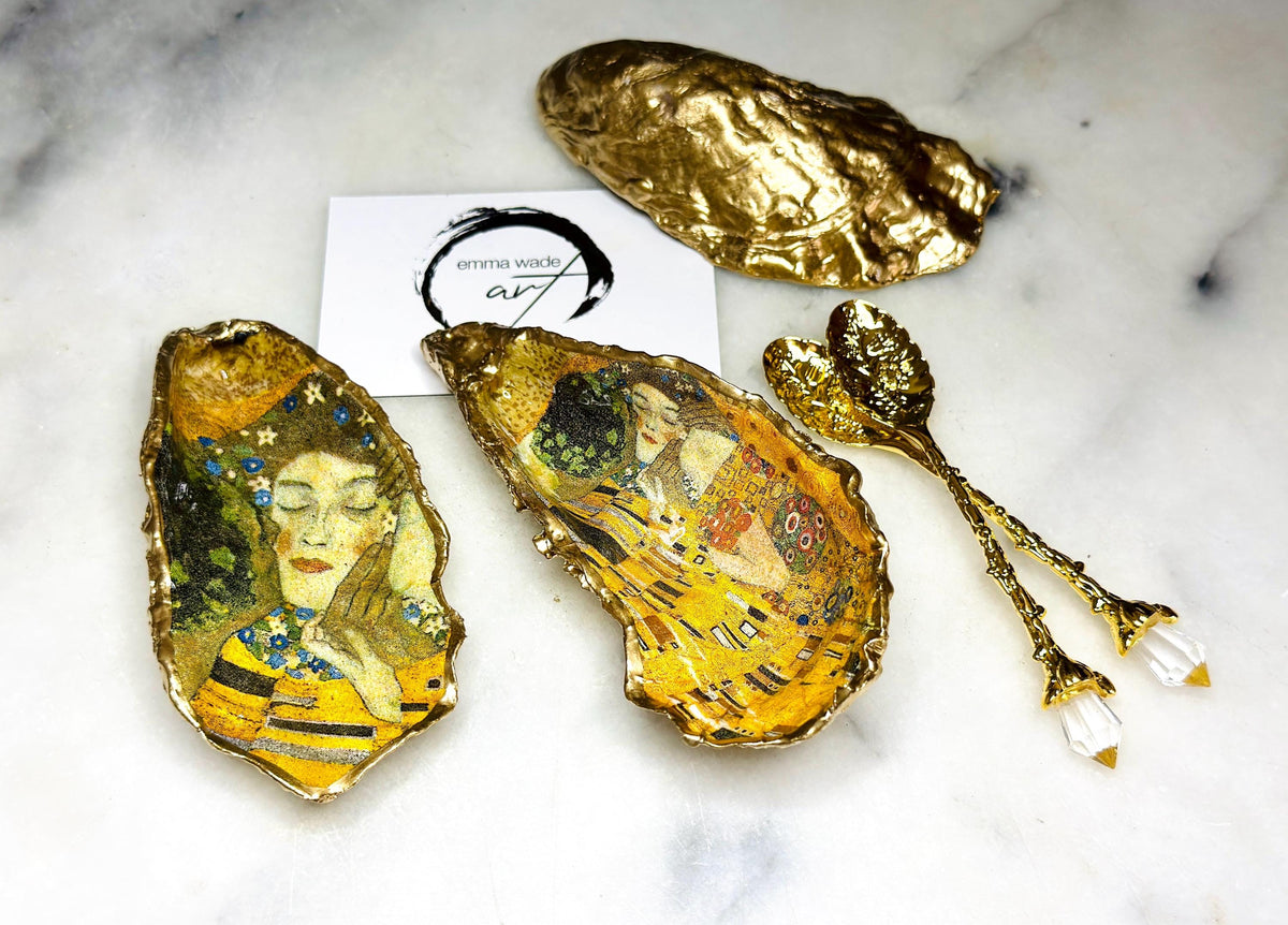 Pair of handmade Dorset oyster shell salt and pepper pinch pots inspired by Gustav Klimt’s The Kiss, decorated with rich gold artwork, hand-finished with liquid gold leaf, and sealed in crystal-hard glossy resin. Luxury coastal serving dishes with optional gold crystal spoons, perfect for weddings, anniversaries, dinner parties, and elegant table décor.