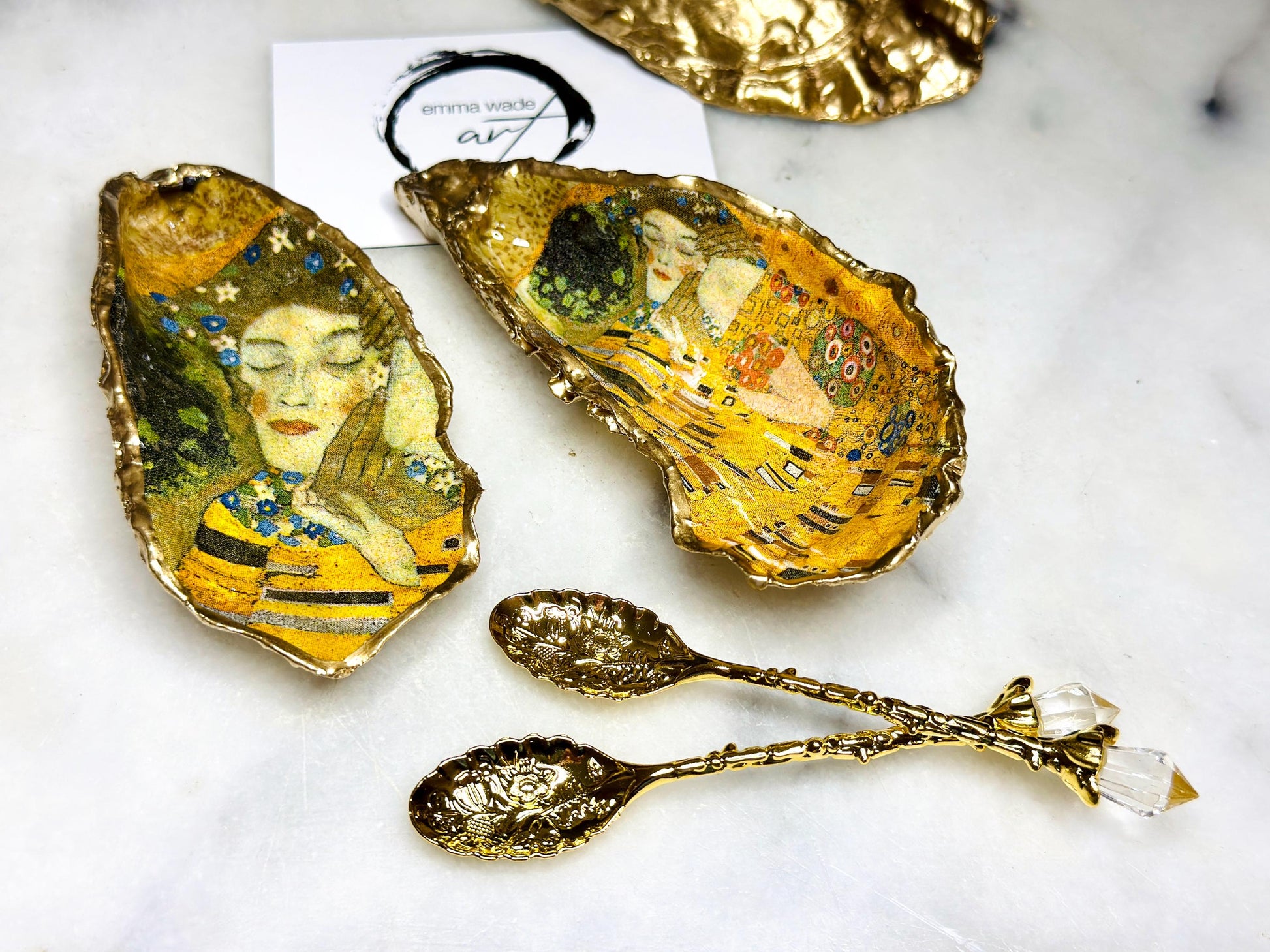 Pair of handmade Dorset oyster shell salt and pepper pinch pots inspired by Gustav Klimt’s The Kiss, decorated with rich gold artwork, hand-finished with liquid gold leaf, and sealed in crystal-hard glossy resin. Luxury coastal serving dishes with optional gold crystal spoons, perfect for weddings, anniversaries, dinner parties, and elegant table décor.