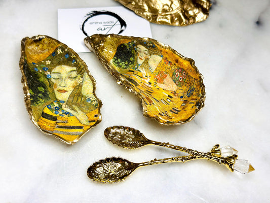 Pair of handmade Dorset oyster shell salt and pepper pinch pots inspired by Gustav Klimt’s The Kiss, decorated with rich gold artwork, hand-finished with liquid gold leaf, and sealed in crystal-hard glossy resin. Luxury coastal serving dishes with optional gold crystal spoons, perfect for weddings, anniversaries, dinner parties, and elegant table décor.