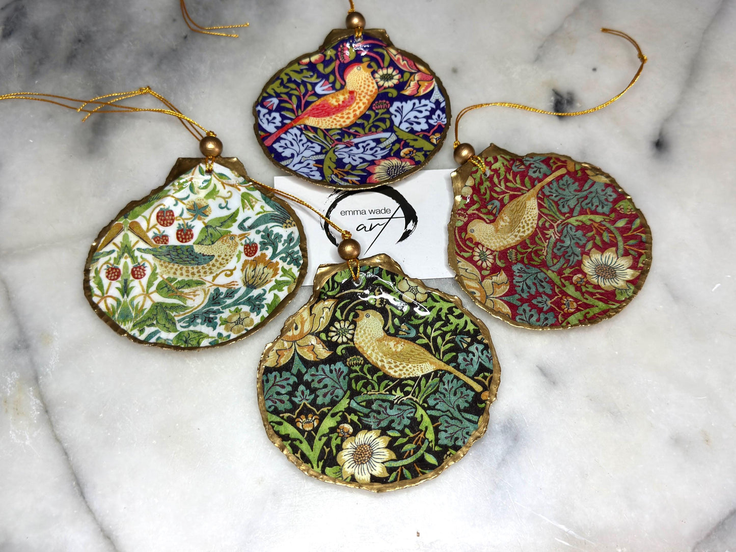 Handmade William Morris Strawberry Thief scallop shell hanging ornaments in four colourways with birds, floral patterns and gold leaf edging. Coastal shell ornaments finished in glossy resin with gold hanging cords for Christmas trees or year-round home decor. UK Heritage Gift
