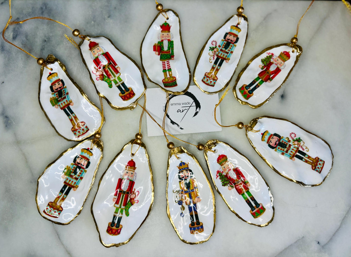 Handmade Nutcracker oyster shell Christmas ornaments with gold gilded edges and glossy resin finish. Traditional festive Nutcracker designs on natural pearl Dorset oyster shells in red, green, aqua, blue and gold tones, styled as luxury coastal Christmas tree decorations.