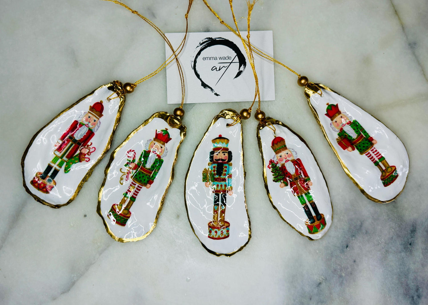 Handmade Nutcracker oyster shell Christmas ornaments with gold gilded edges and glossy resin finish. Traditional festive Nutcracker designs on natural pearl Dorset oyster shells in red, green, aqua, blue and gold tones, styled as luxury coastal Christmas tree decorations.