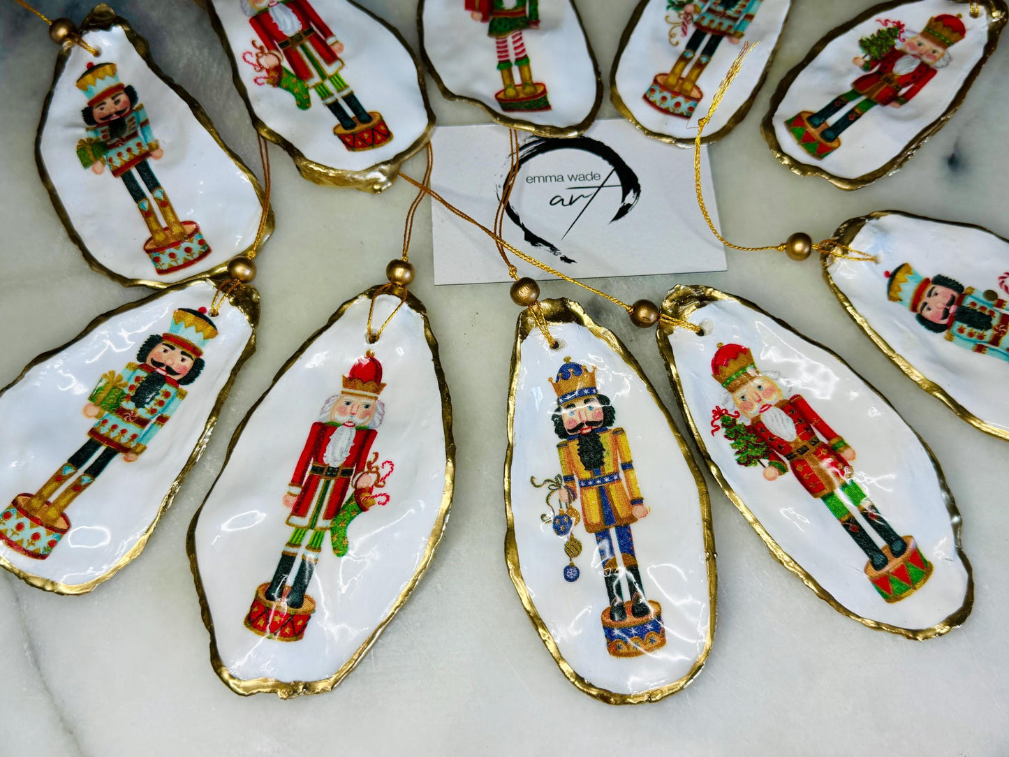 Handmade Nutcracker oyster shell Christmas ornaments with gold gilded edges and glossy resin finish. Traditional festive Nutcracker designs on natural pearl Dorset oyster shells in red, green, aqua, blue and gold tones, styled as luxury coastal Christmas tree decorations.