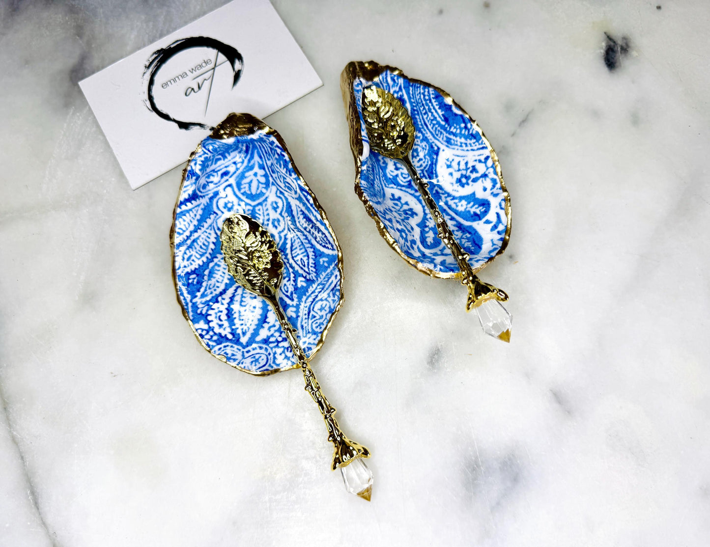 Blue and white paisley oyster shell salt cellar set with gold leaf edging and matching gold crystal spoons. Handmade Dorset oyster shell pinch pots finished in glossy food safe resin. Coastal dining decor and luxury beach house table accessory.