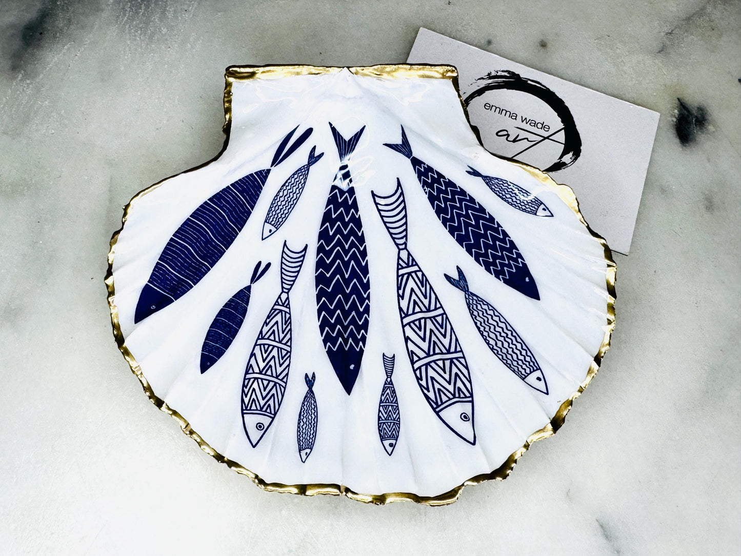 Handmade Dorset scallop shell trinket dishes featuring elegant blue fish illustrations with hand-painted gold leaf edging and glossy crystal clear resin. Coastal nautical jewellery dishes inspired by Scandinavian ocean decor, styled on a neutral background with detailed blue fish artwork and luxurious gilded edges.