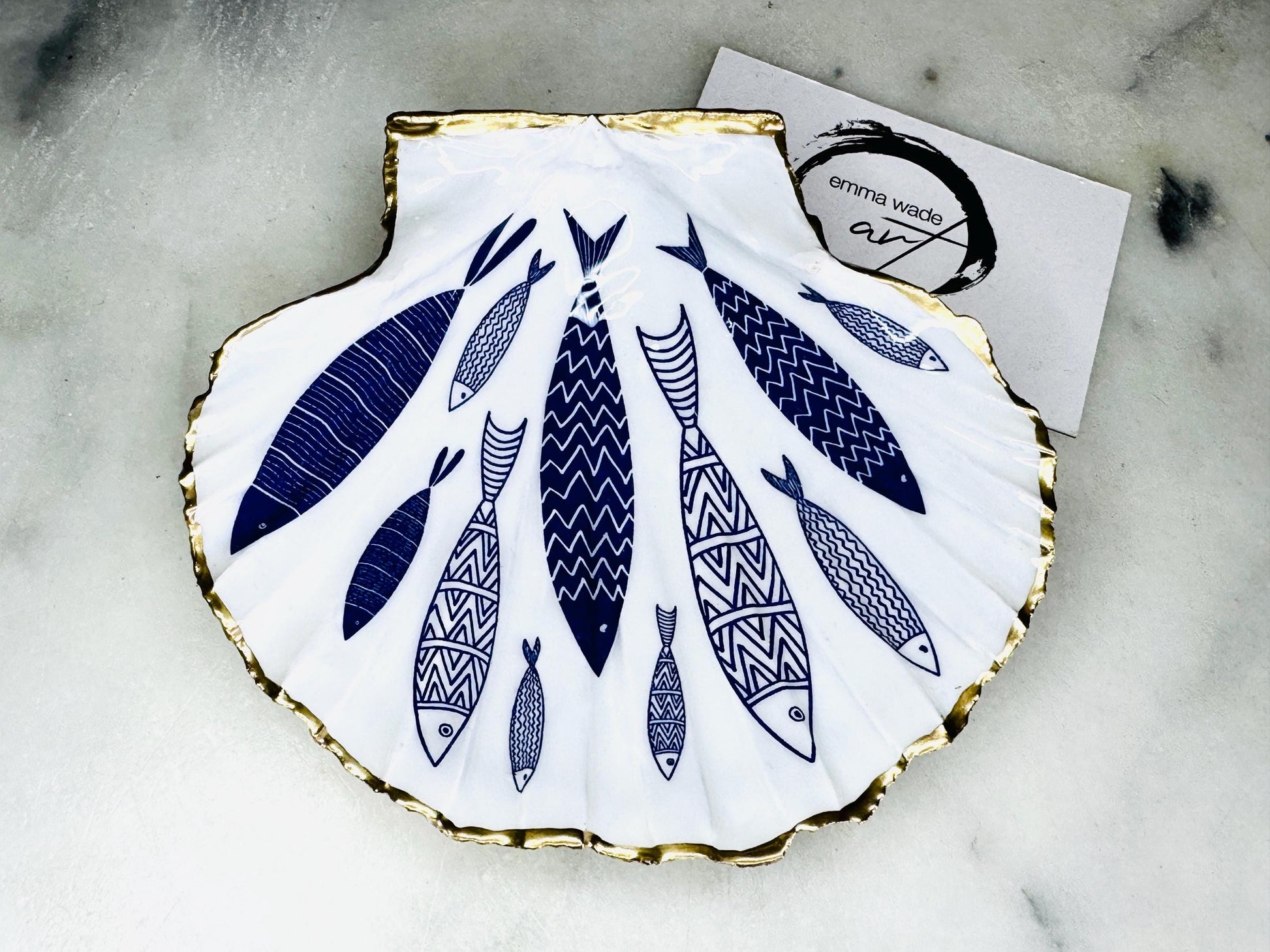Handmade Dorset scallop shell trinket dishes featuring elegant blue fish illustrations with hand-painted gold leaf edging and glossy crystal clear resin. Coastal nautical jewellery dishes inspired by Scandinavian ocean decor, styled on a neutral background with detailed blue fish artwork and luxurious gilded edges.