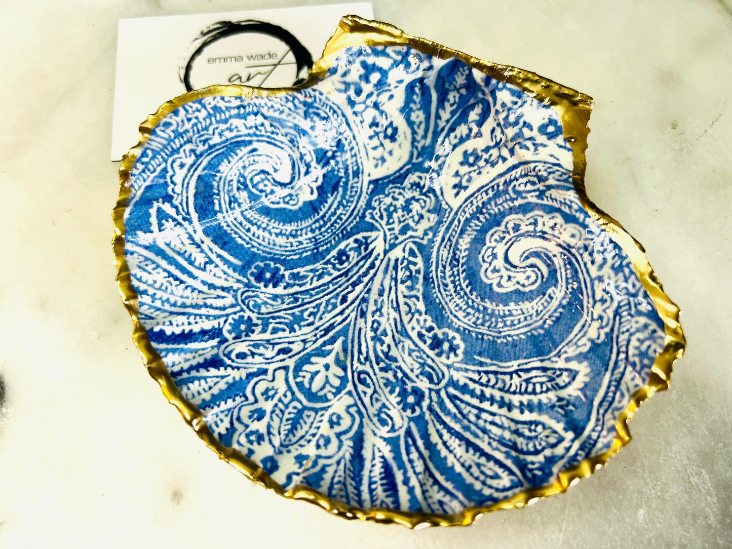 Blue and white paisley scallop shell ring catcher with hand applied gold leaf edging and glossy resin finish. Handmade Dorset shell jewellery tray styled with pearls on a marble background. Coastal vanity decor and luxury beach house accessory gift.