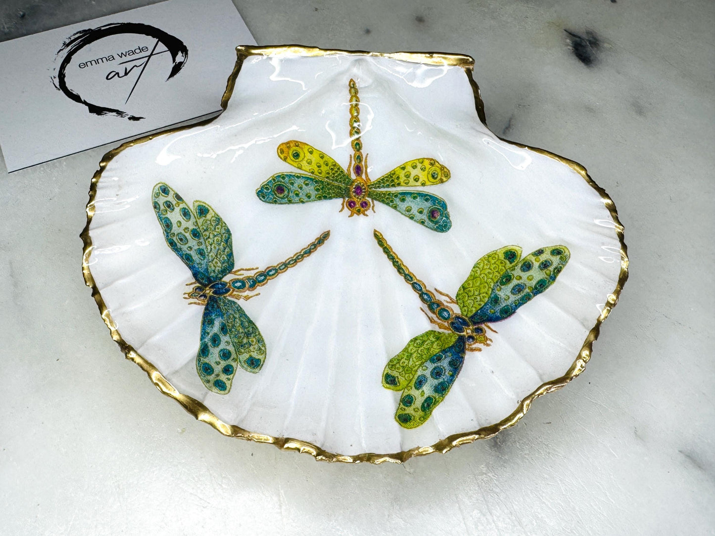 Handmade dragonfly scallop shell trinket dish with gold leaf edging and glossy resin finish. Coastal jewellery and ring dish crafted from a natural Dorset scallop shell, featuring colourful dragonfly artwork. Decorative shell bowl photographed on a light background, showing the natural shell shape and shimmering gilded edges, ideal for holding rings, earrings, trinkets or small treasures.