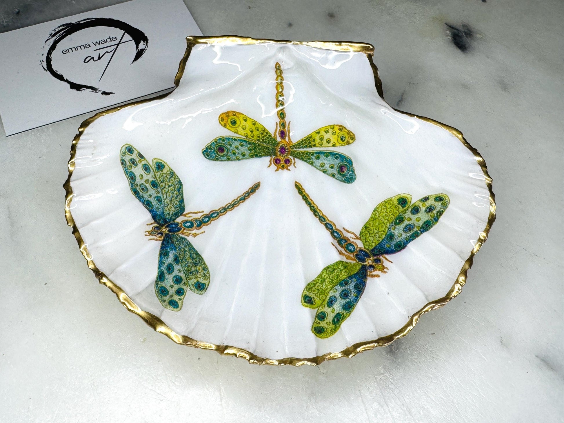 Handmade dragonfly scallop shell trinket dish with gold leaf edging and glossy resin finish. Coastal jewellery and ring dish crafted from a natural Dorset scallop shell, featuring colourful dragonfly artwork. Decorative shell bowl photographed on a light background, showing the natural shell shape and shimmering gilded edges, ideal for holding rings, earrings, trinkets or small treasures.