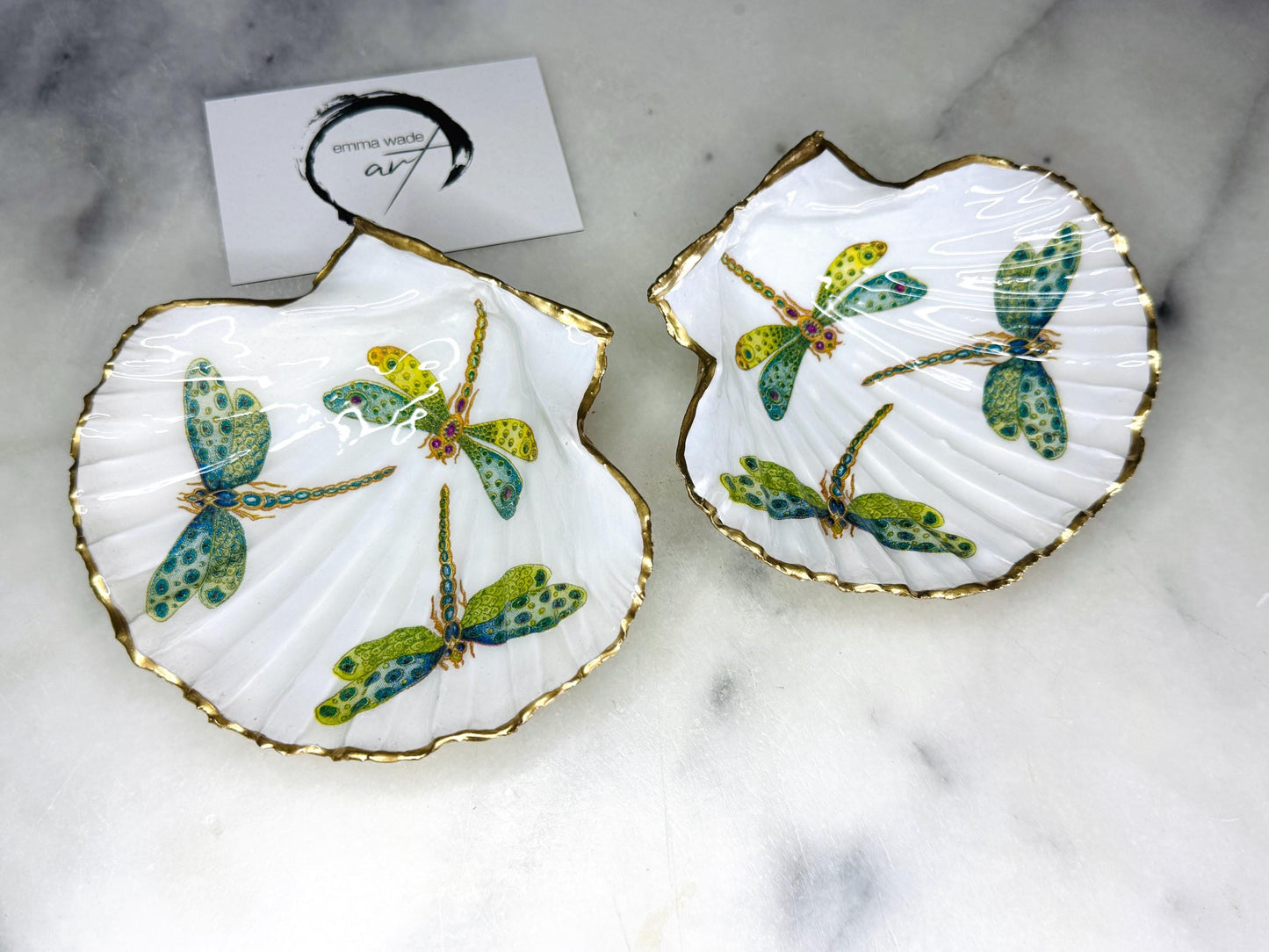 Handmade dragonfly scallop shell trinket dish with gold leaf edging and glossy resin finish. Coastal jewellery and ring dish crafted from a natural Dorset scallop shell, featuring colourful dragonfly artwork. Decorative shell bowl photographed on a light background, showing the natural shell shape and shimmering gilded edges, ideal for holding rings, earrings, trinkets or small treasures.
