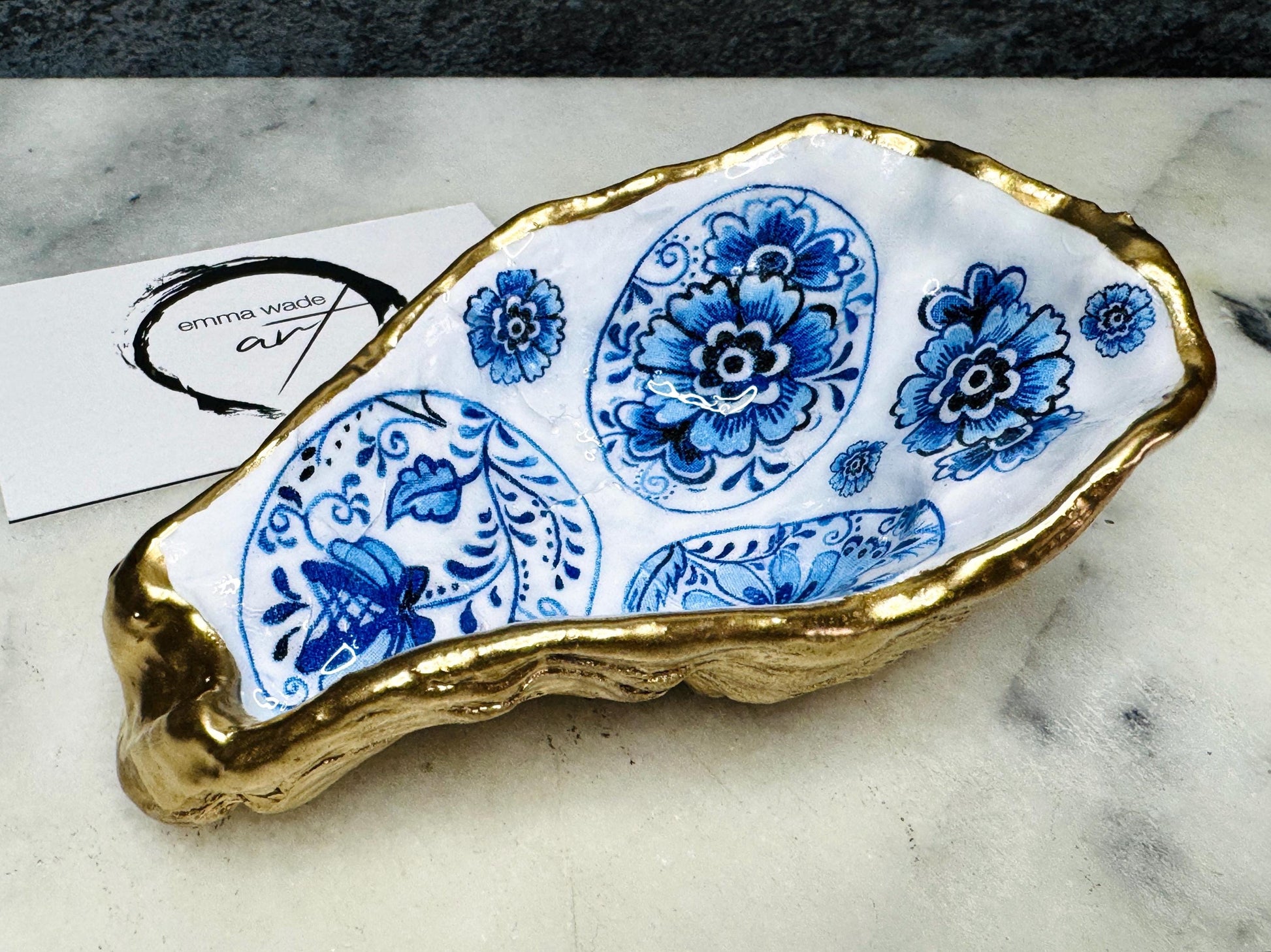 Handmade Dorset oyster shell dish featuring a blue and white patterned egg design with vintage style detailing. Finished with real gold leaf and epoxy resin for durability. Unique oyster shell jewellery dish, trinket holder, salt and pepper pinch pot, tea light holder, or spoon rest. A coastal décor ornament and gift idea for birthdays, weddings, anniversaries, or Christmas. Sustainable handmade UK oyster shell art.