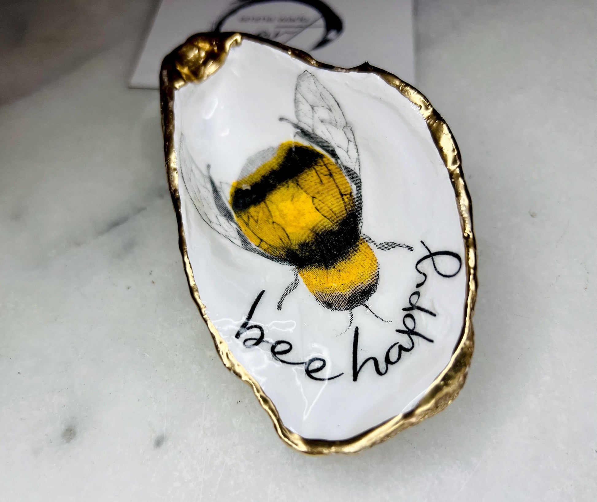 bee happy oyster shell trinket dish, Dorset oyster shell jewellery holder, handmade bee design coastal decor, gold leaf gilded oyster shell ornament, sustainable oyster shell dish UK, bumble bee oyster shell jewellery tray, nature inspired bee oyster shell gift, eco friendly oyster shell bathroom accessory, oyster shell salt and pepper pinch pot, unique bee themed oyster shell keepsake, handmade Dorset oyster shell decor, bee lover jewellery dish gift, coastal oyster shell art UK