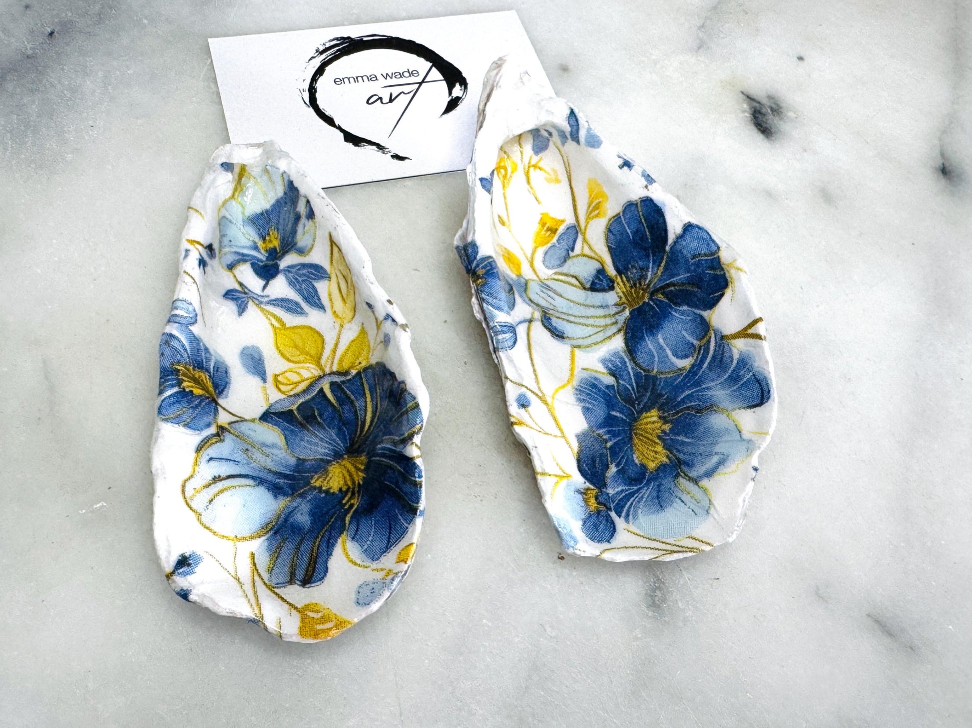 Handmade blue and yellow floral oyster shell salt and pepper dishes shown as a matching pair, crafted from natural Dorset shells and styled with small gold spoons. Coastal-inspired pinch pots featuring a decorative floral design with natural shell backs, perfect for table decor, weddings, or a unique hostess gift. Each shell is one of a kind, finished by hand, and ideal for adding colour and elegance to a dining table.