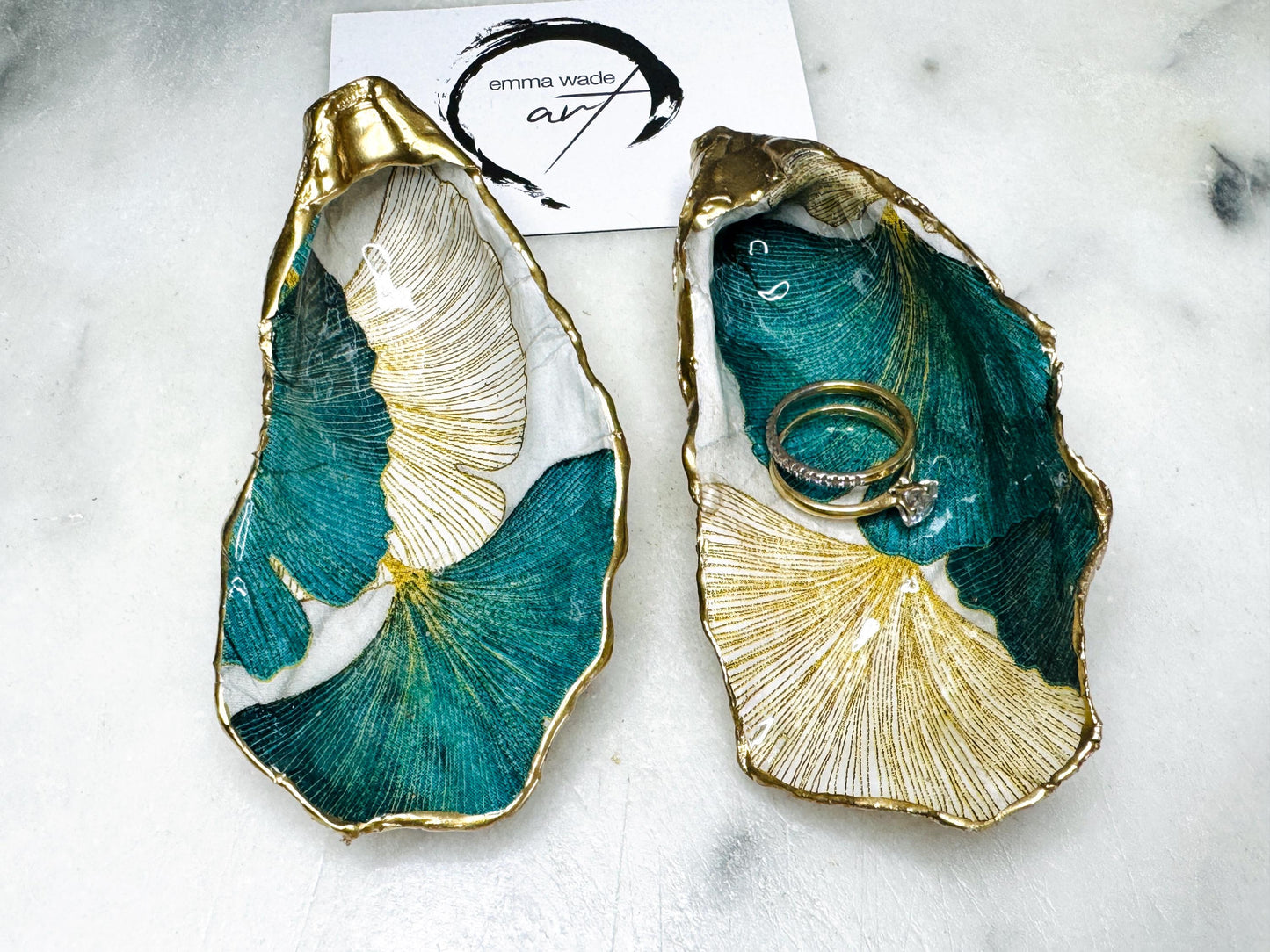Handmade Dorset oyster shell ring dish featuring Japanese Ginkgo floral leaf artwork in emerald green, gold, and pearl tones with hand-applied liquid gold leaf edging. Luxury coastal jewellery tray sealed in glossy crystal-clear epoxy resin, styled with gold rings.