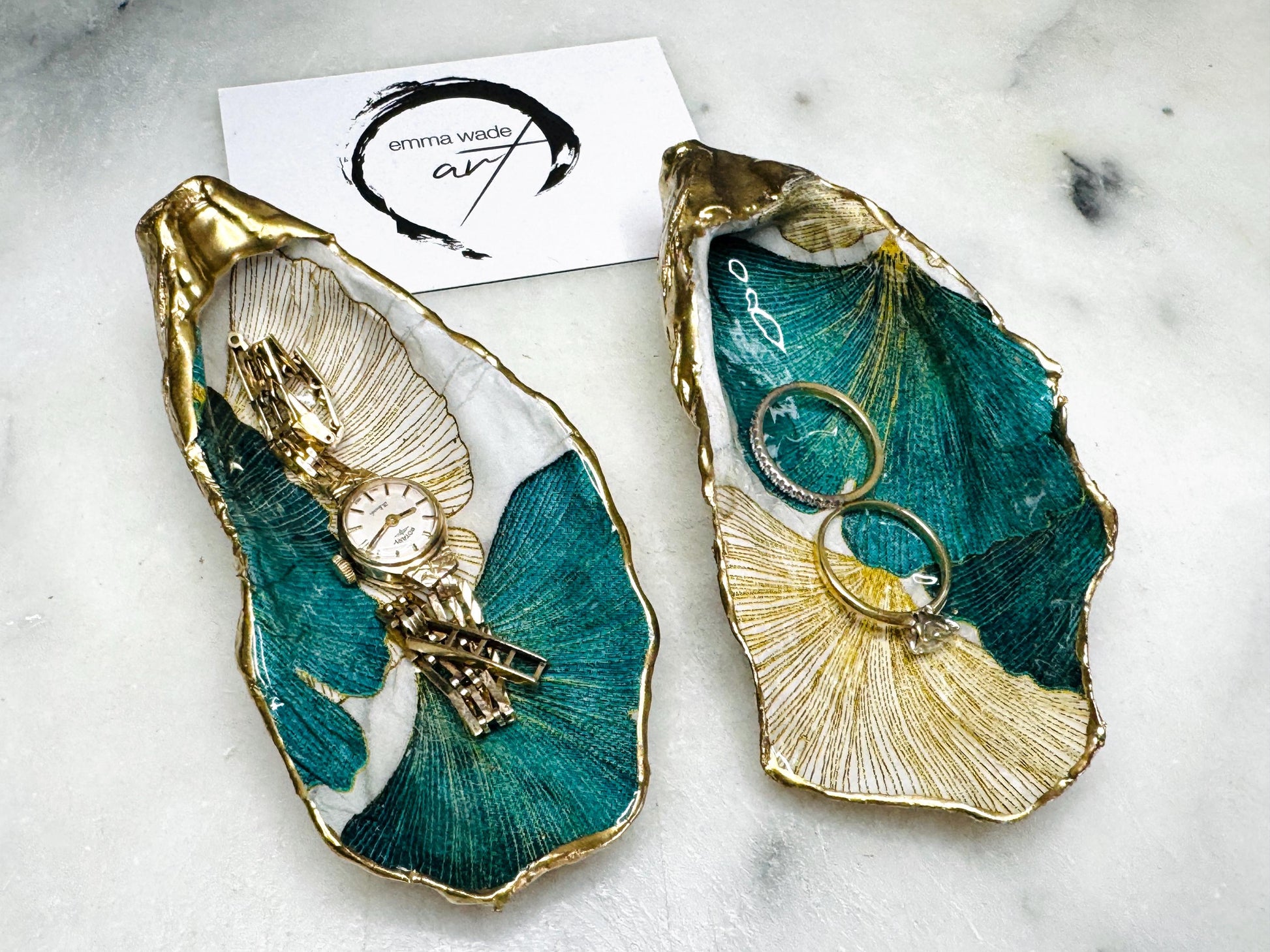 Handmade Dorset oyster shell ring dish featuring Japanese Ginkgo floral leaf artwork in emerald green, gold, and pearl tones with hand-applied liquid gold leaf edging. Luxury coastal jewellery tray sealed in glossy crystal-clear epoxy resin, styled with gold rings.