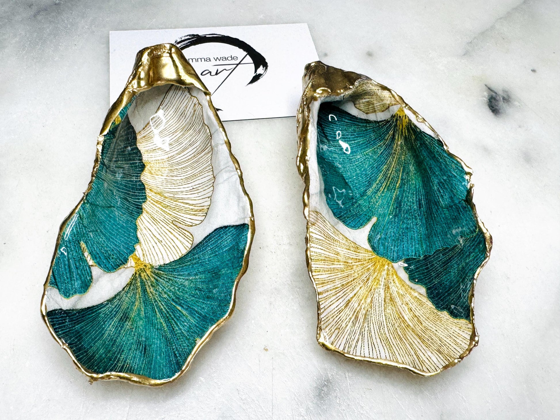 Handmade Dorset oyster shell ring dish featuring Japanese Ginkgo floral leaf artwork in emerald green, gold, and pearl tones with hand-applied liquid gold leaf edging. Luxury coastal jewellery tray sealed in glossy crystal-clear epoxy resin, styled with gold rings.