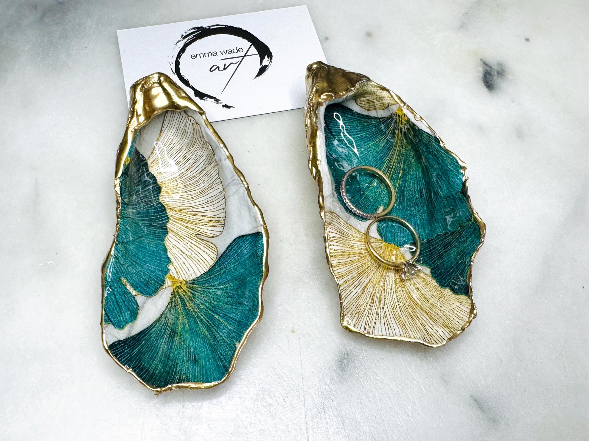 Handmade Dorset oyster shell ring dish featuring Japanese Ginkgo floral leaf artwork in emerald green, gold, and pearl tones with hand-applied liquid gold leaf edging. Luxury coastal jewellery tray sealed in glossy crystal-clear epoxy resin, styled with gold rings.