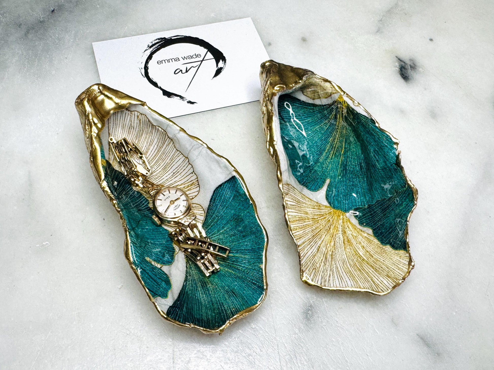 Handmade Dorset oyster shell ring dish featuring Japanese Ginkgo floral leaf artwork in emerald green, gold, and pearl tones with hand-applied liquid gold leaf edging. Luxury coastal jewellery tray sealed in glossy crystal-clear epoxy resin, styled with gold rings.