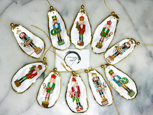 Handmade Nutcracker oyster shell Christmas ornaments with gold gilded edges and glossy resin finish. Traditional festive Nutcracker designs on natural pearl Dorset oyster shells in red, green, aqua, blue and gold tones, styled as luxury coastal Christmas tree decorations.